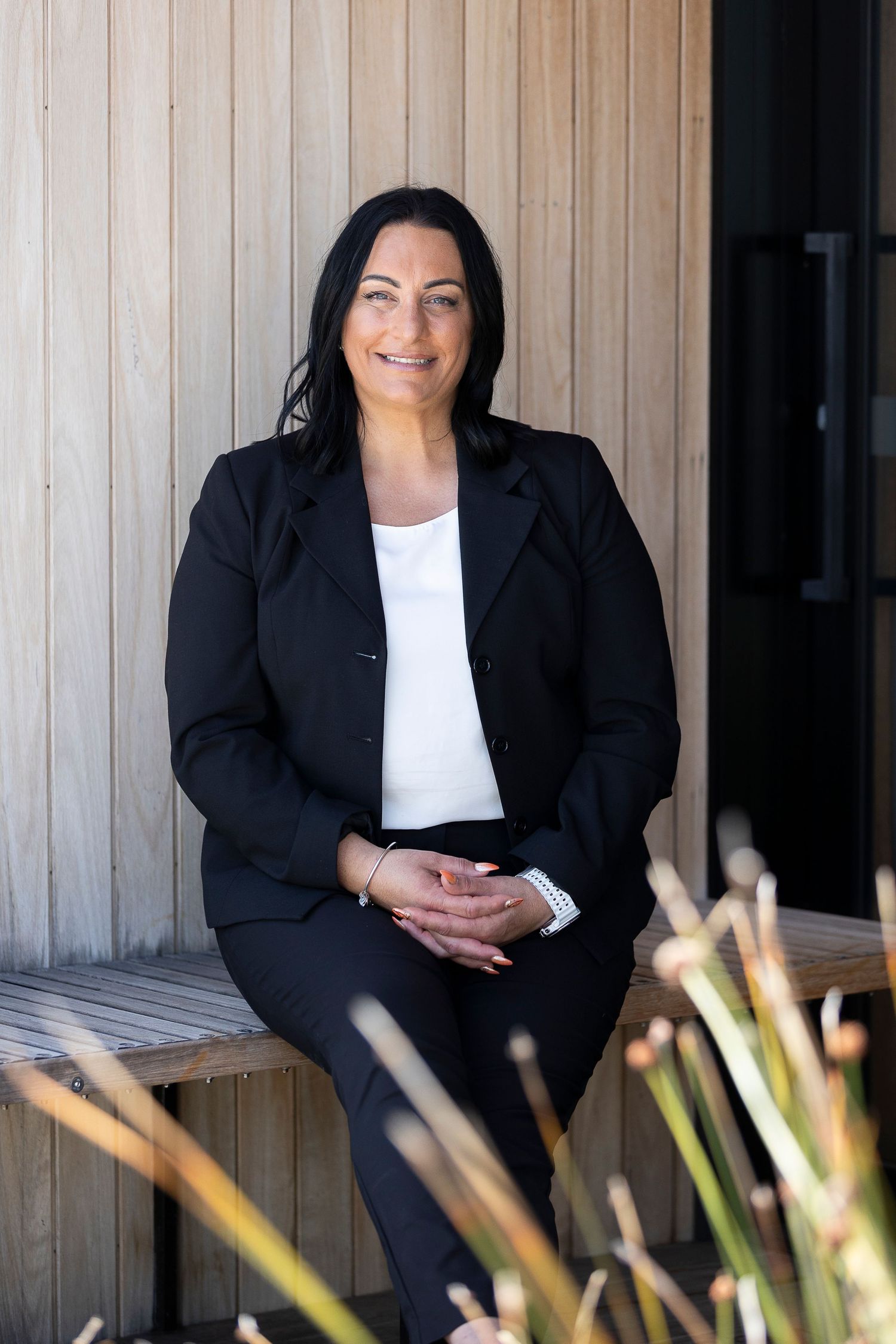 Business professional in dark blazer seated against wooden wall background.
