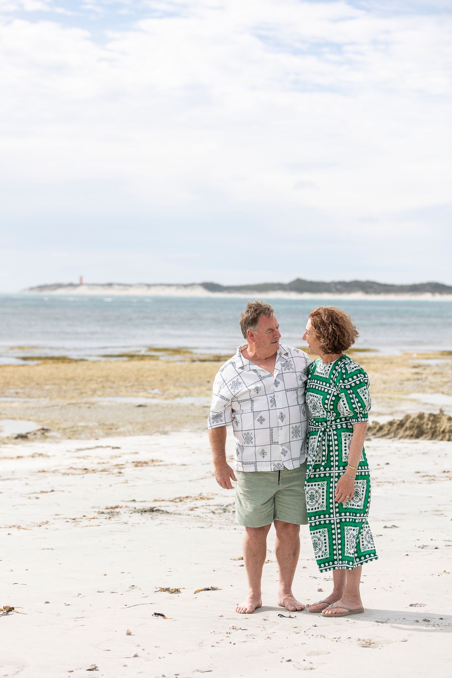 Couple sitting together on white sandy beach overlooking the ocean.