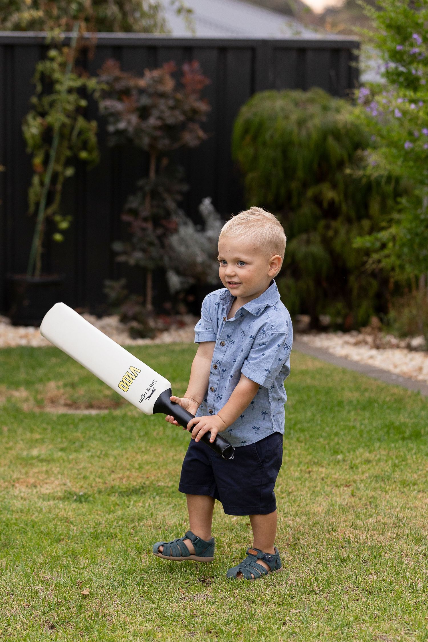 Small child playing on grass with a white bottle in a casual denim outfit.