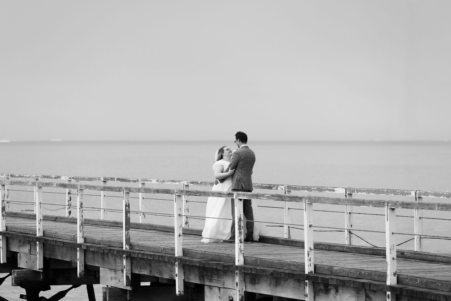 A romantic silhouette of a couple standing together on a long wooden pier.