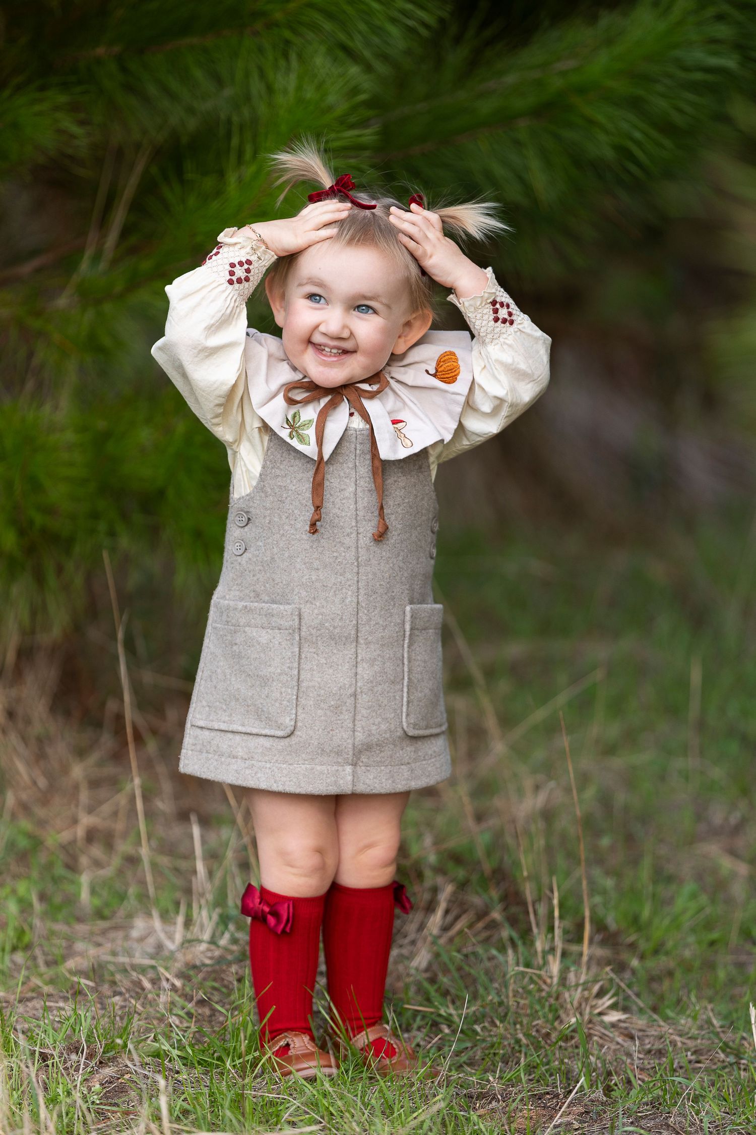 Toddler in grey dress and red knee socks smiling while playing outdoors.