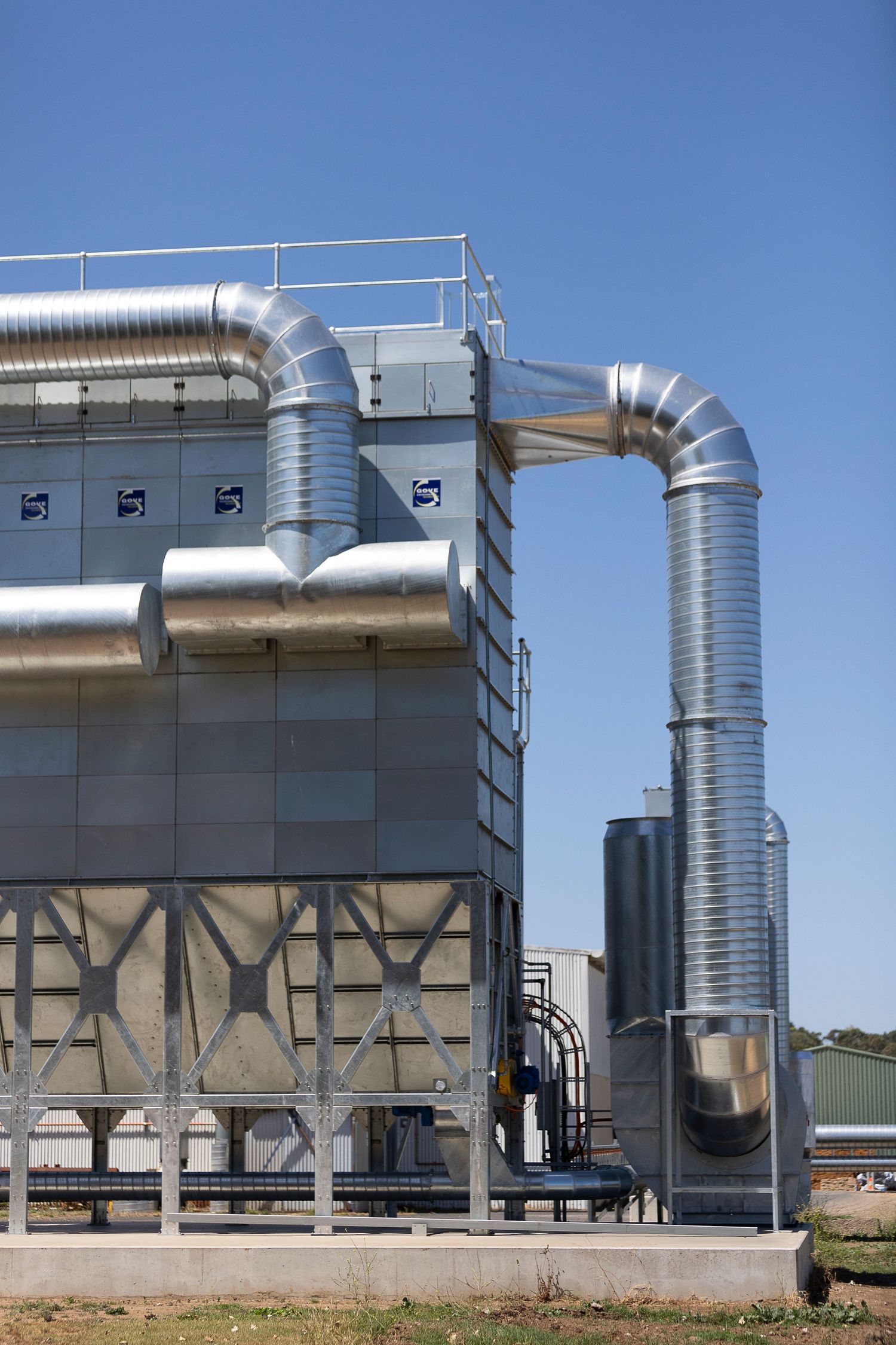 Large industrial dust collection systems with silver ductwork against blue sky.