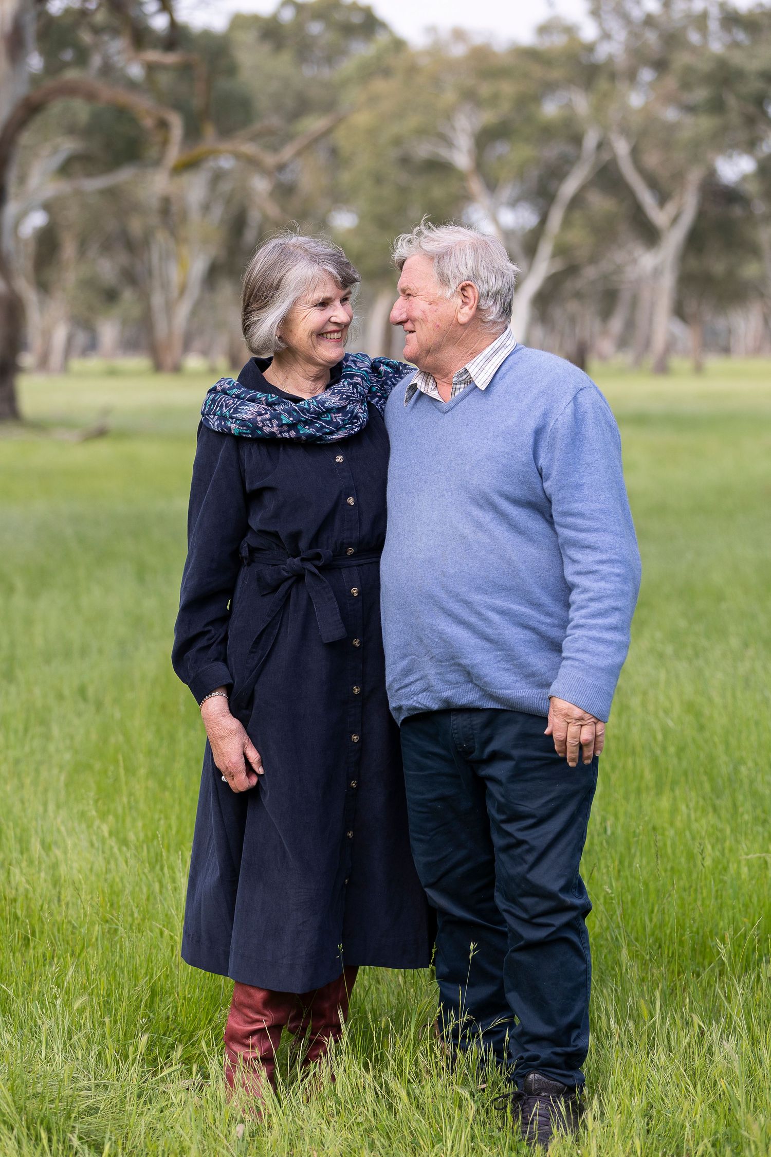A couple shares a tender moment while standing in tall grass with trees in the background.