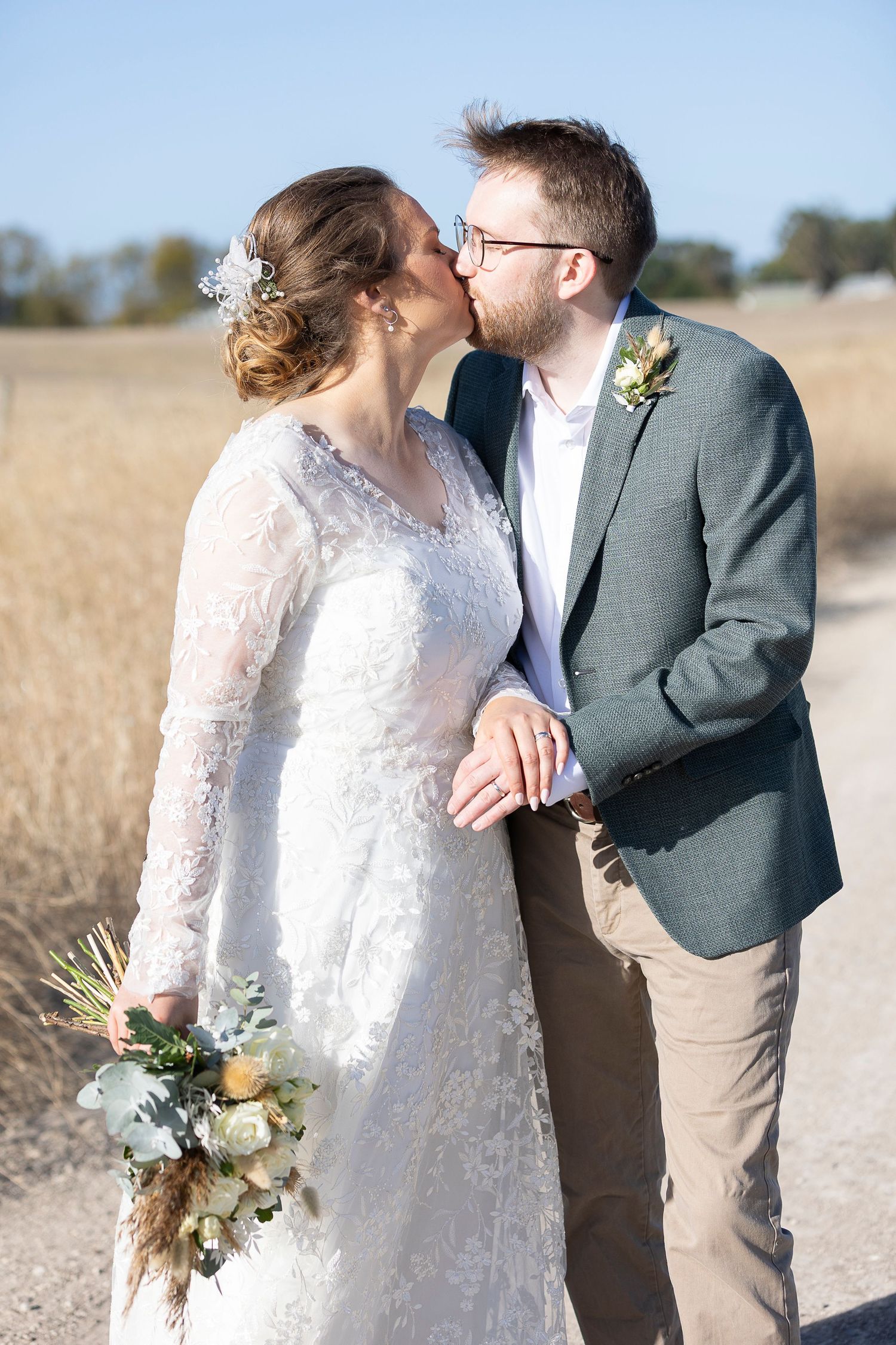 Romantic wedding couple shares intimate moments in a sunlit field.