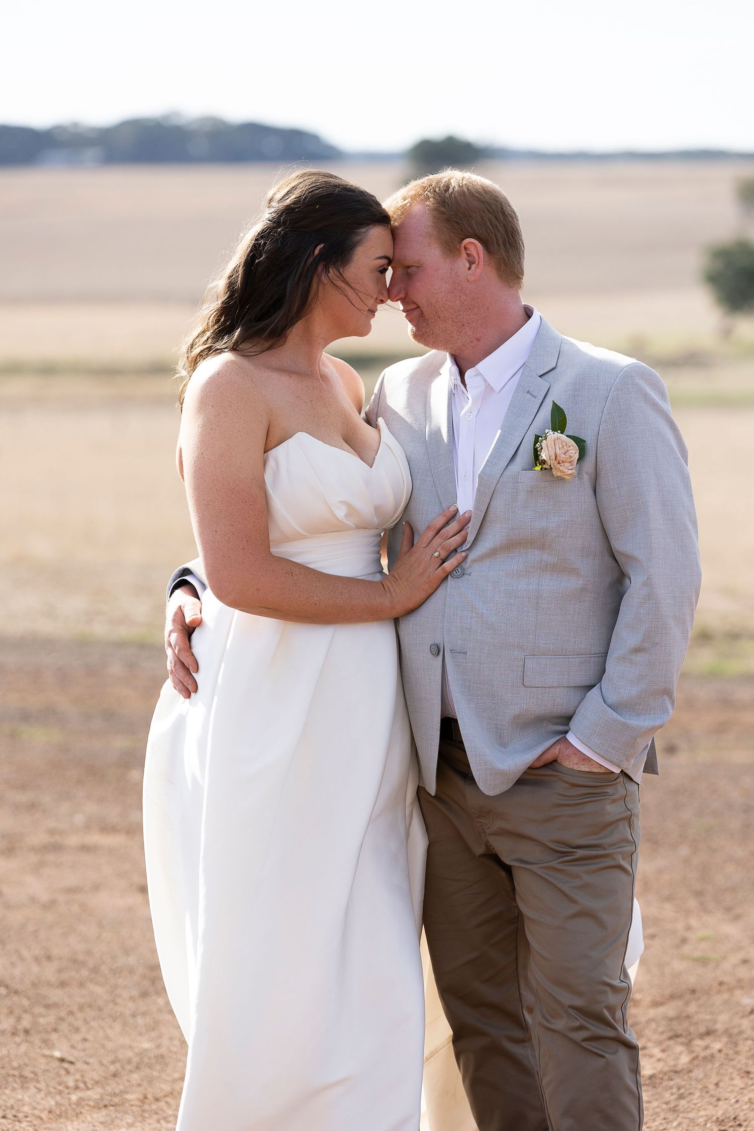 Couple in wedding attire sharing an intimate moment in a field.