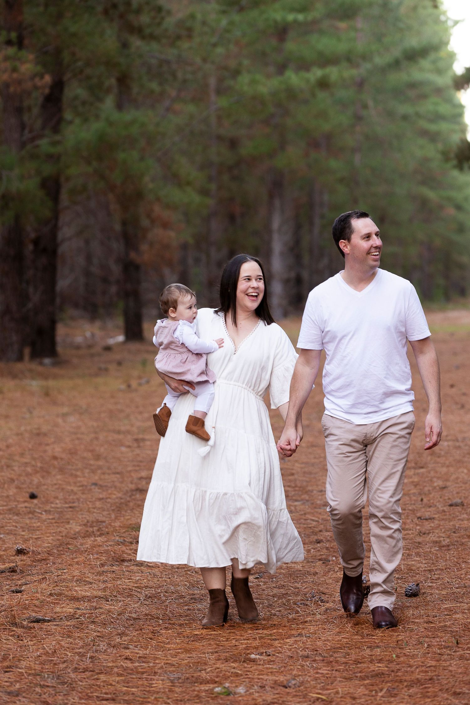 Family walking together through a pine forest wearing coordinated white and beige outfits.