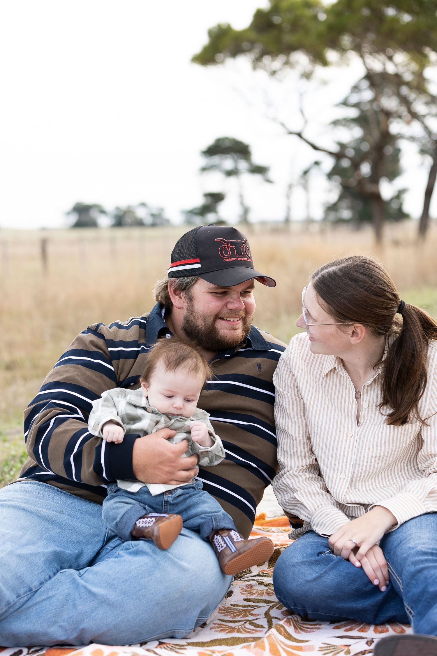 A couple having a romantic picnic in a grassy field with trees in the background.