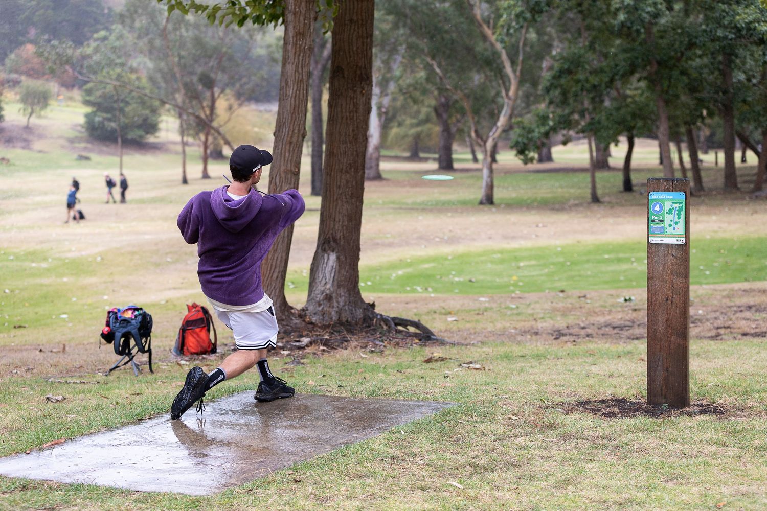 People exercising and enjoying outdoor activities in a park with trees and walking paths.
