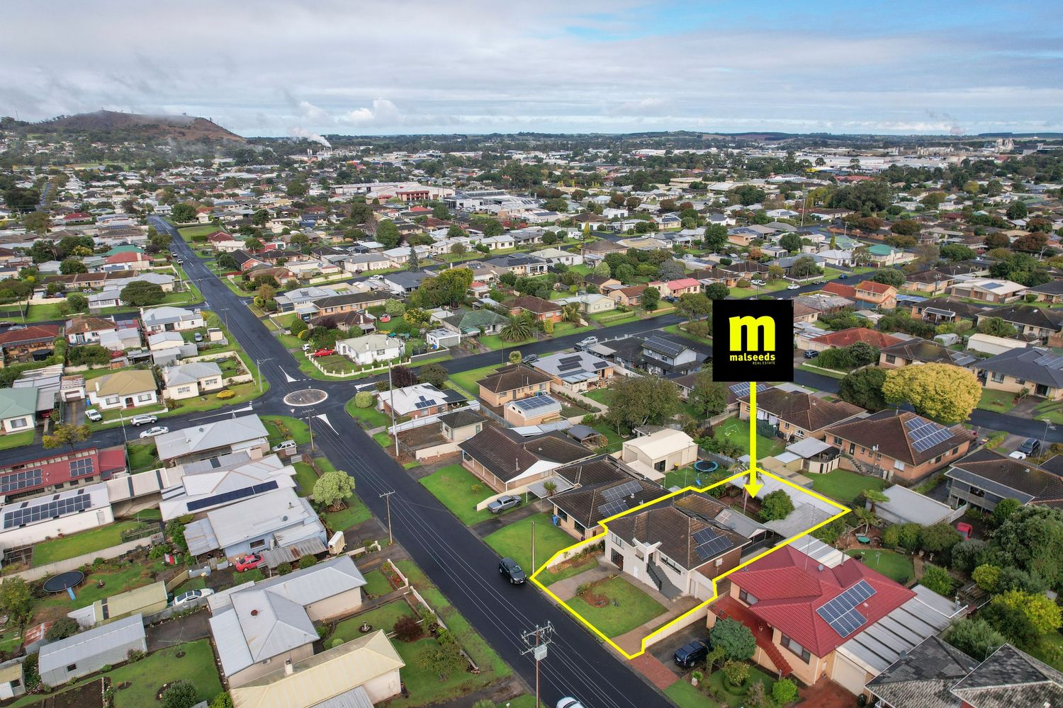 Aerial view of a suburban neighborhood with a highlighted property marked by a real estate sign amid residential streets.