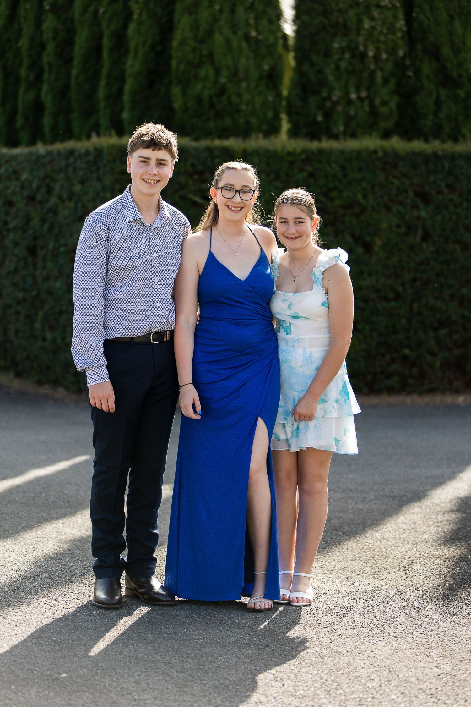 Group photo outdoors wearing formal attire against hedge backdrop.