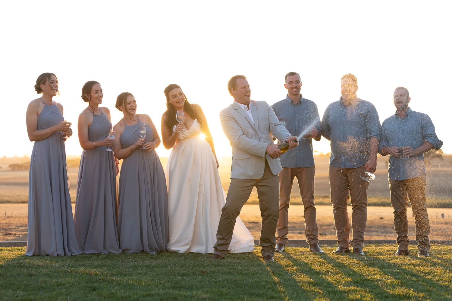 Wedding party poses together at sunset with bridesmaids in blue dresses.