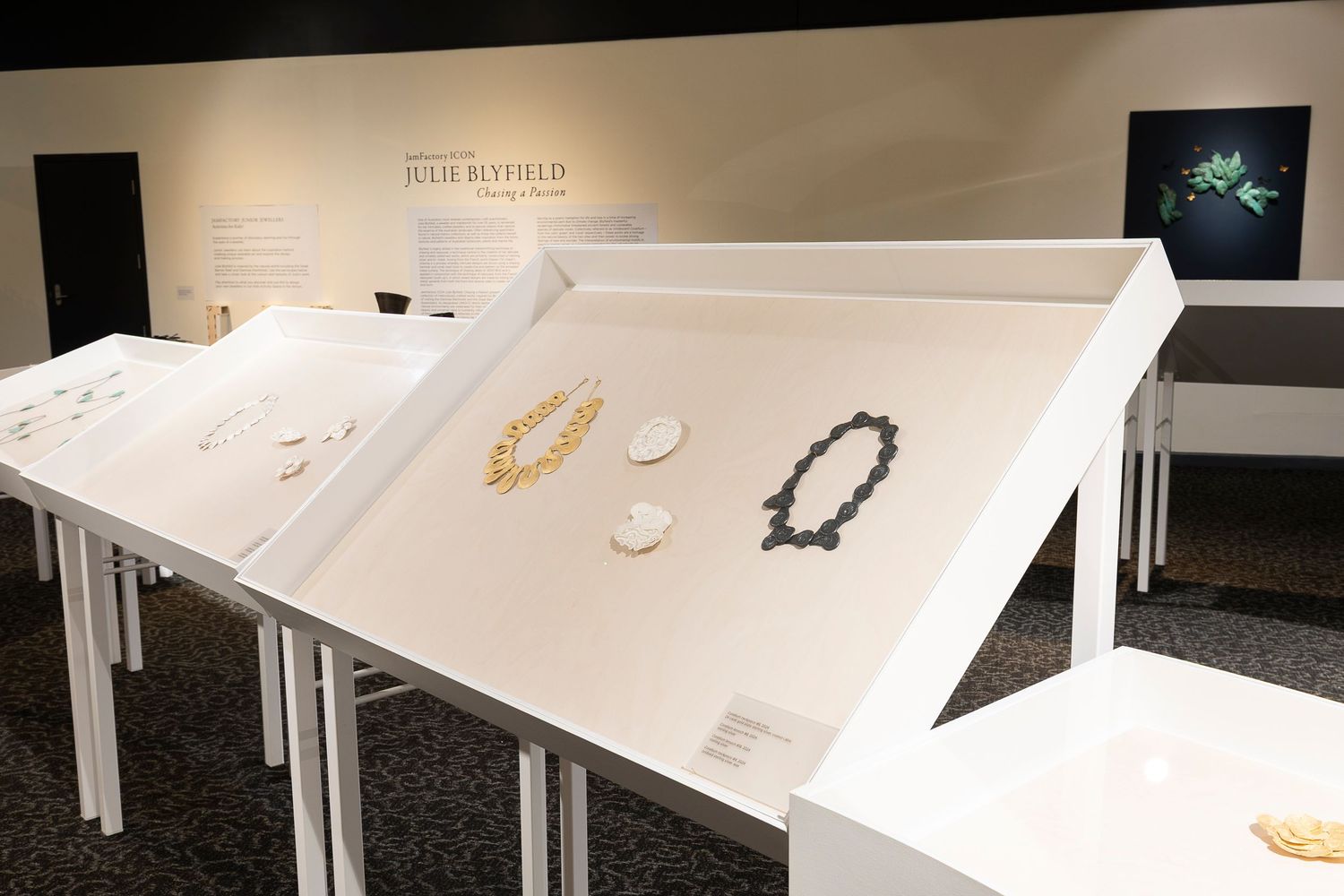 Museum exhibit with curved white display tables showcasing jewelry and small objects.