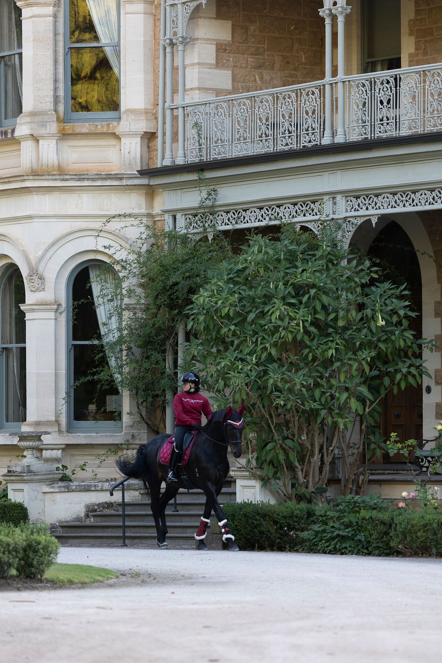 Equestrians with horses outside historic mansion with ornate balconies.