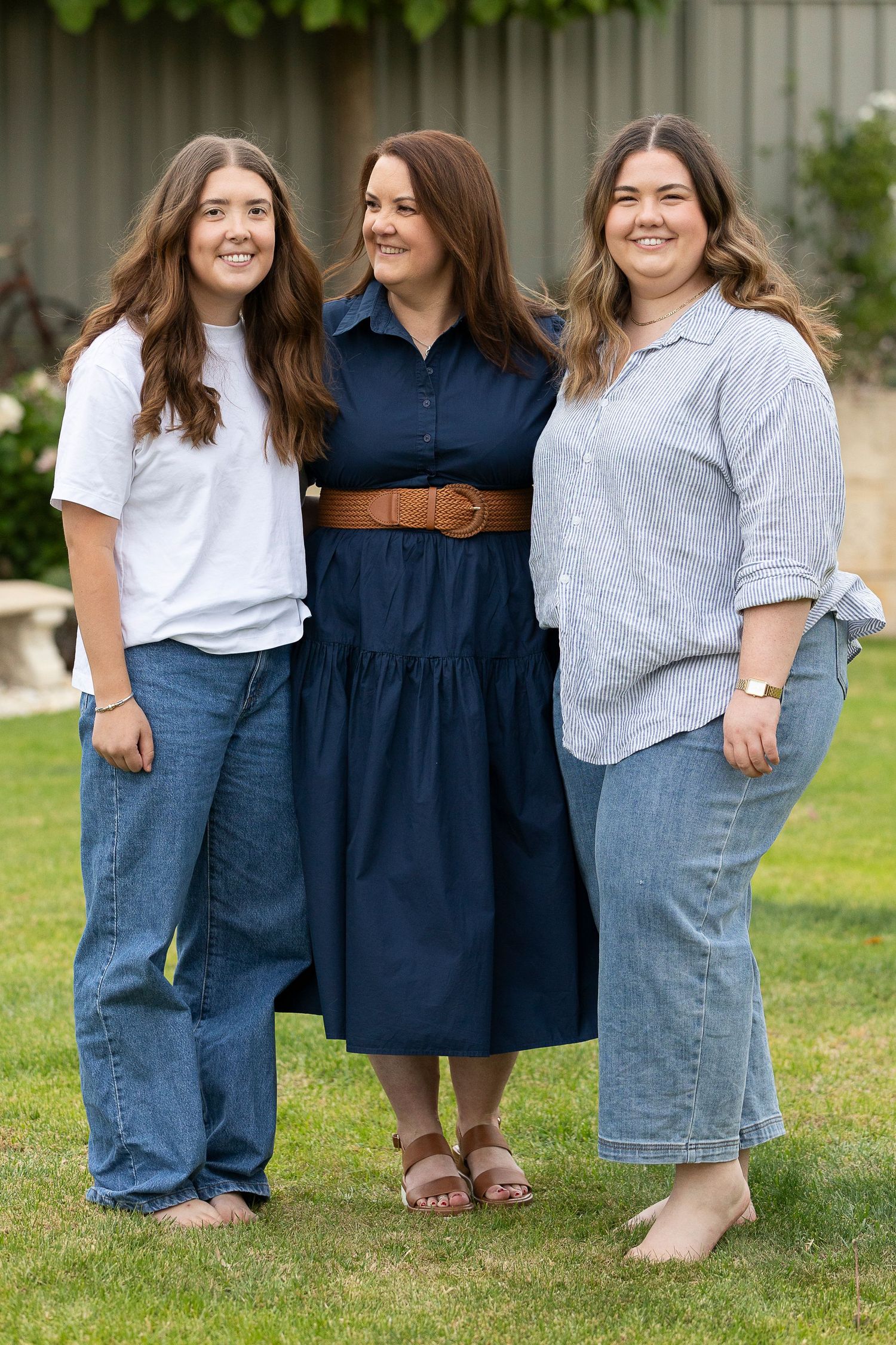 Three friends in casual outfits pose together on green grass in a coordinated outdoor photoshoot.