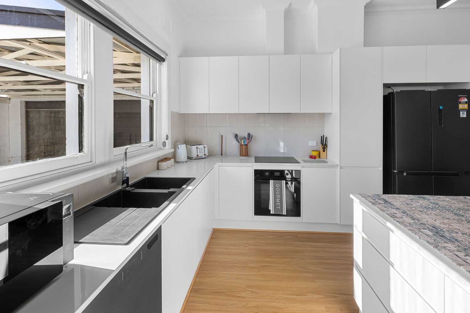 Modern white kitchen with black appliances, granite countertop, induction cooktop, and timber floors in a bright open layout.