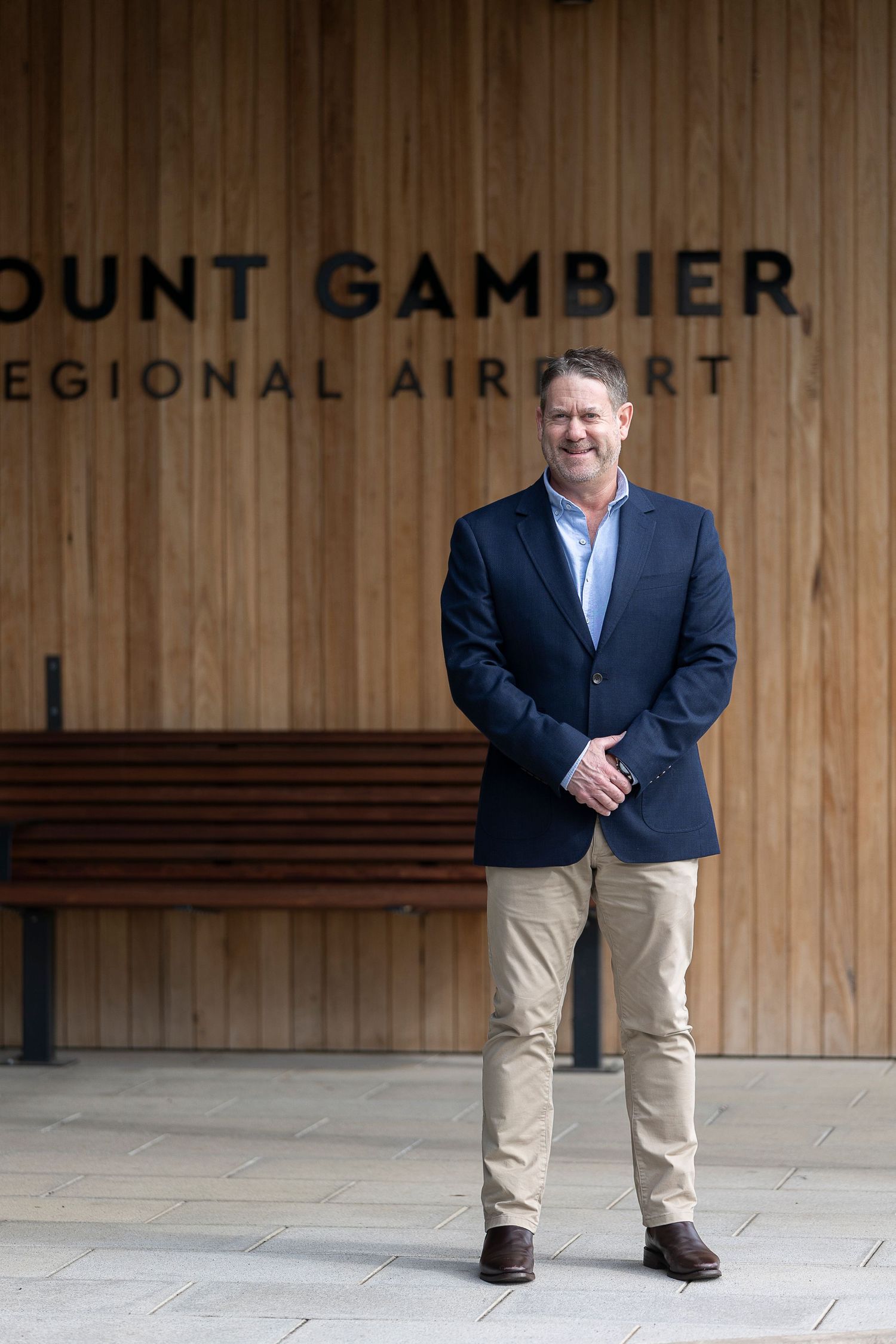 Man in navy blazer smiling outside Mount Gambier Regional Airport entrance with wooden facade.