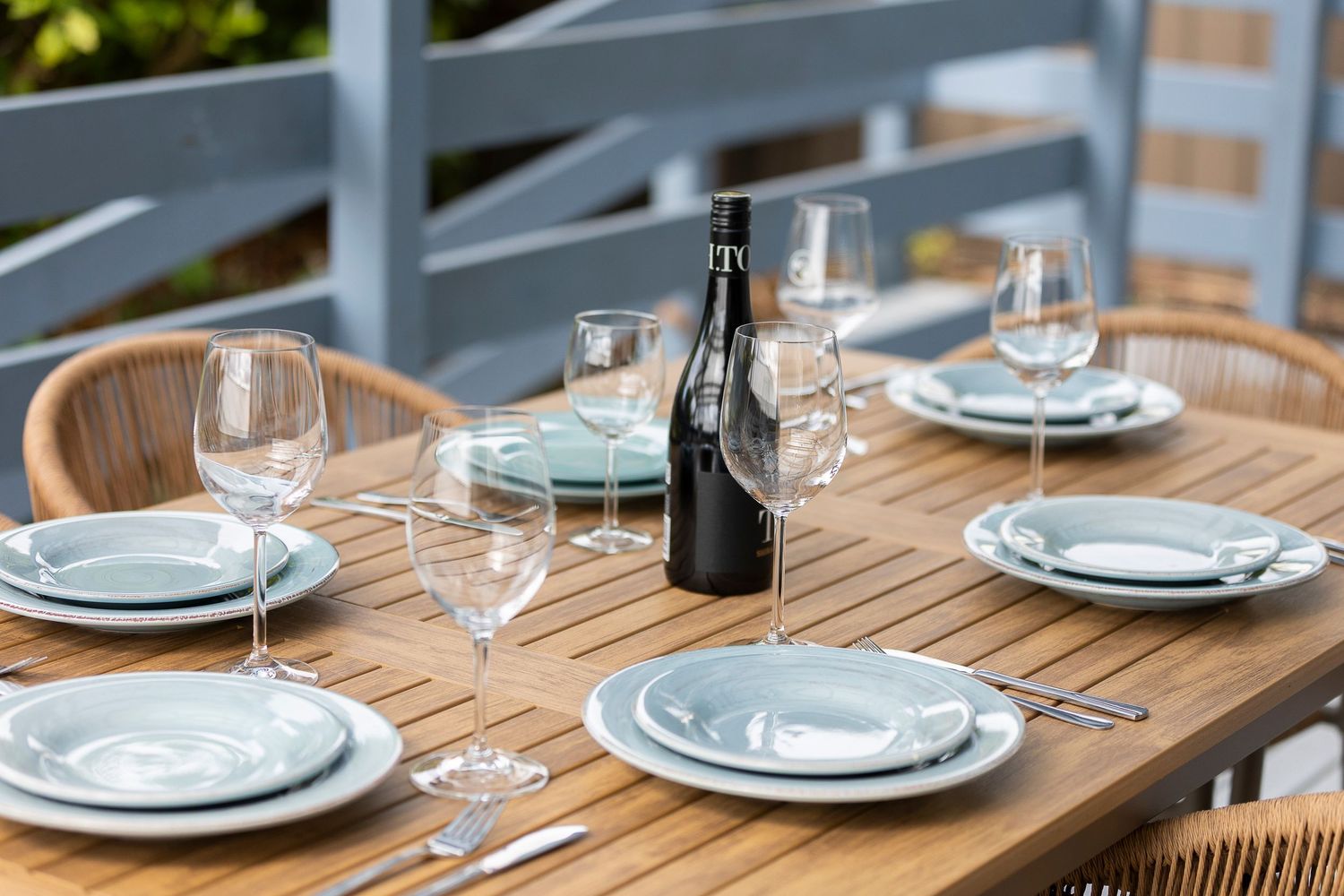 Outdoor wooden dining table set with wine glasses, plates, and a wine bottle for an elegant al fresco dining experience.