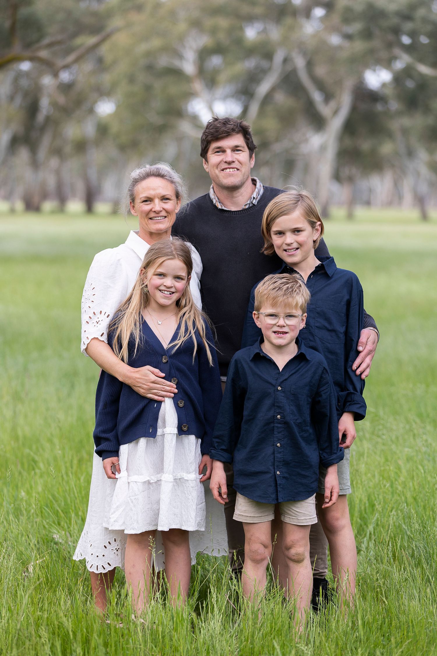 Family group in coordinated navy and white outfits poses together in tall grass.