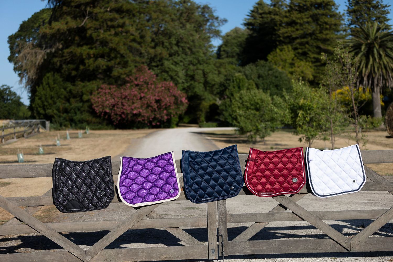 Row of colorful saddle pads displayed outdoors against a natural background.