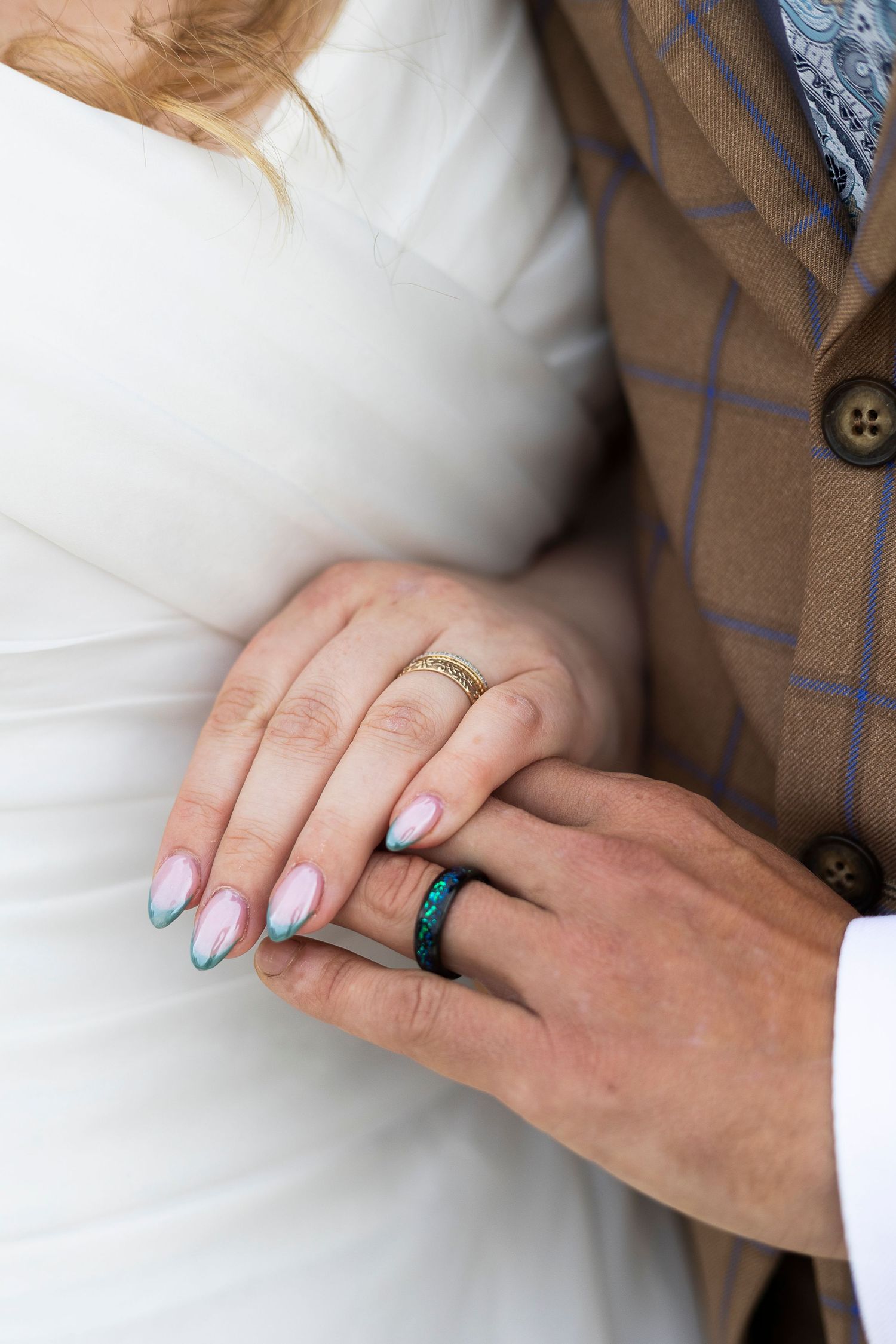 Close-up of hands showing wedding rings against white dress fabric.
