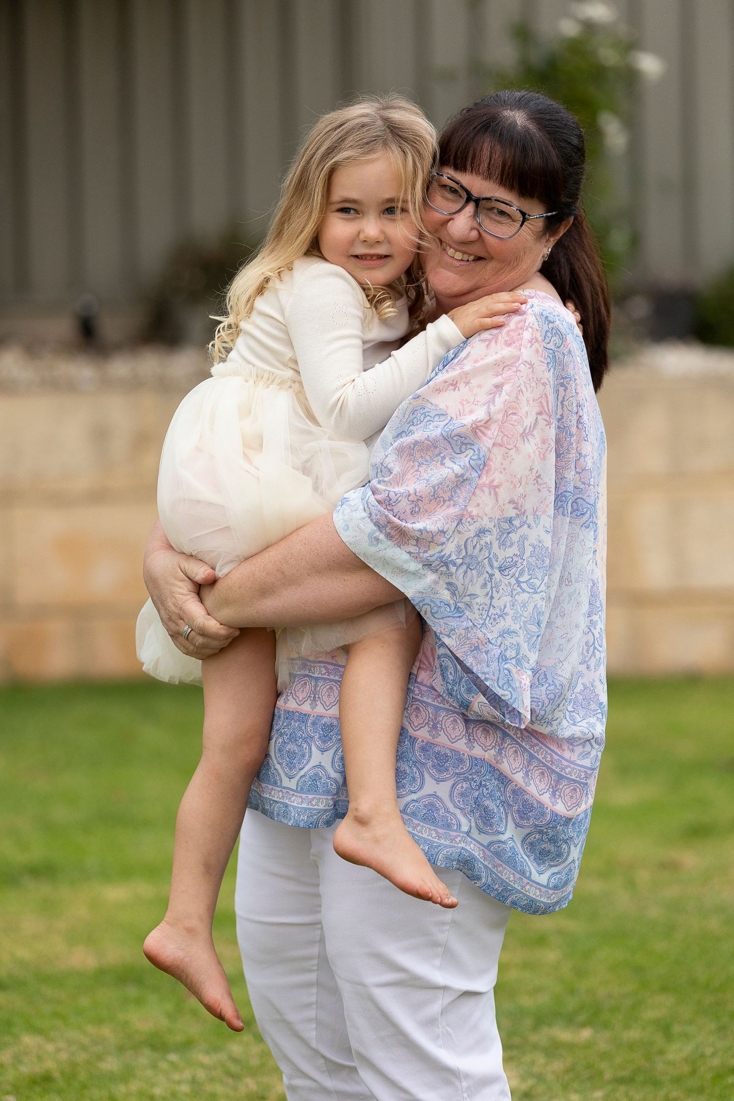 Parent holding child in floral dress against outdoor background.