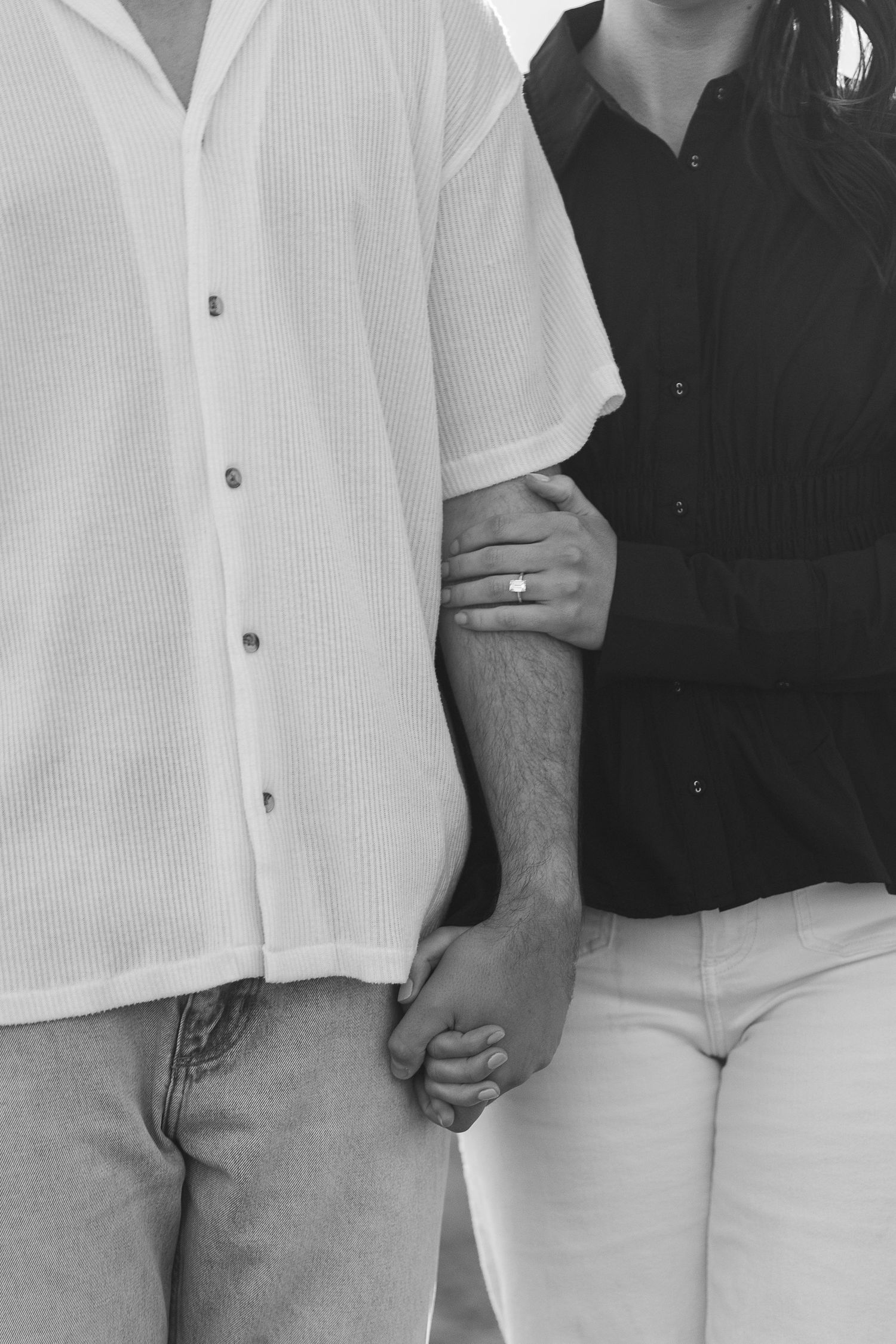 Black and white close-up of two people holding hands, wearing contrasting light and dark button-down shirts.