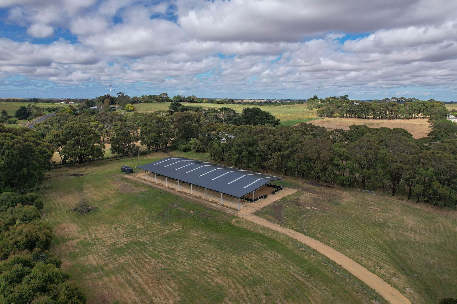 Aerial view of solar panels installed on a rural property surrounded by green fields and trees under cloudy skies.