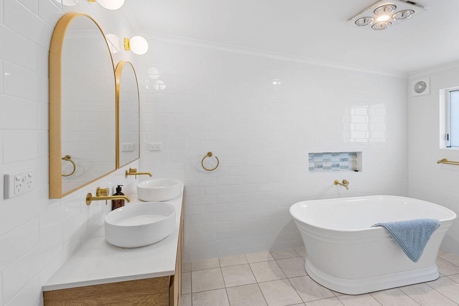Luxurious bathroom featuring a freestanding oval tub, gold-framed mirror, and white tile flooring.