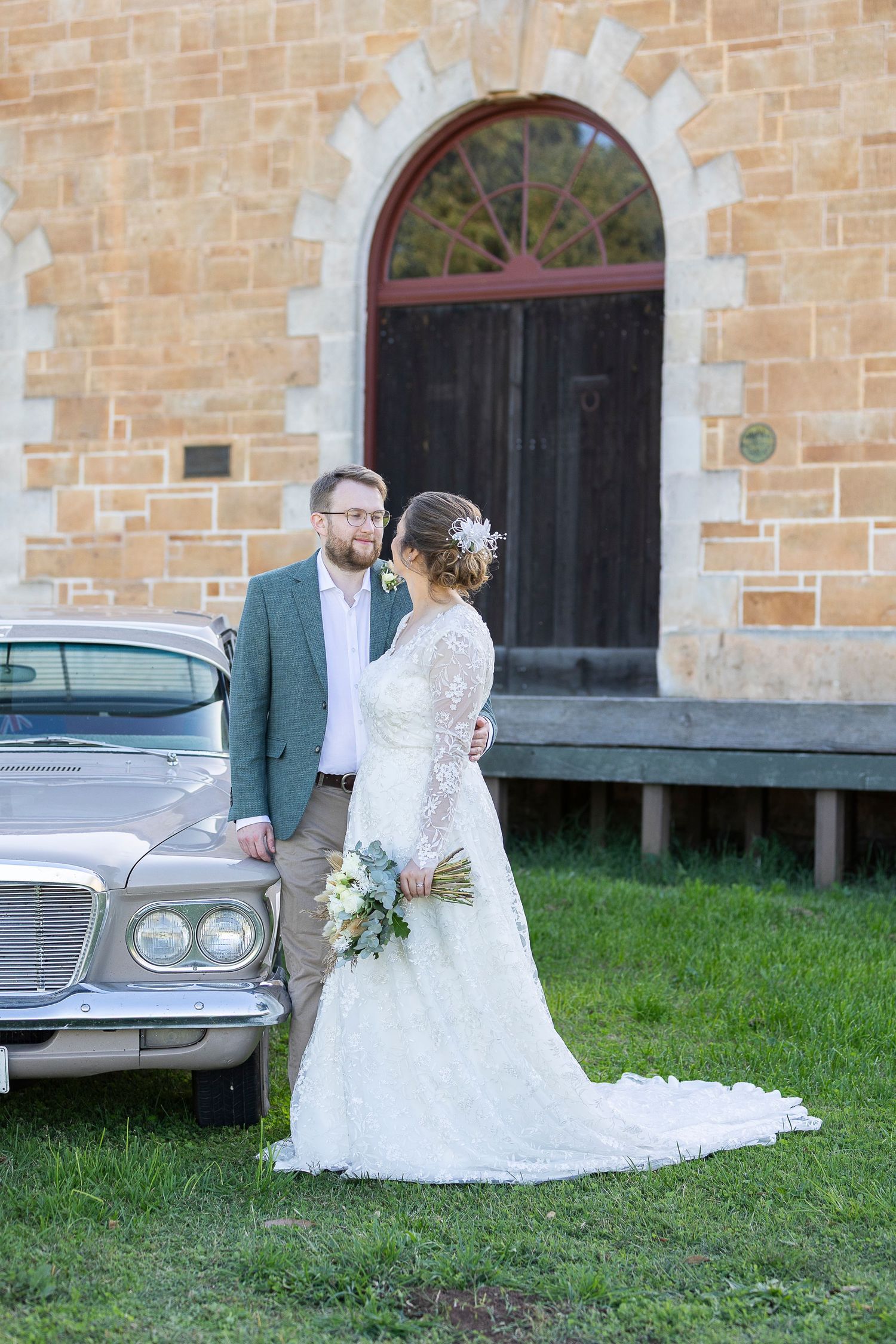 Wedding portraits taken outside historic stone building with vintage car in background.