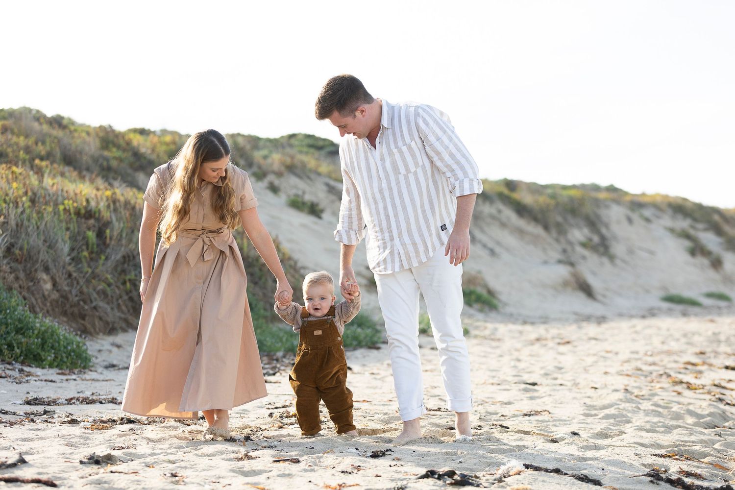 A family walks together on a sandy beach path during golden hour.