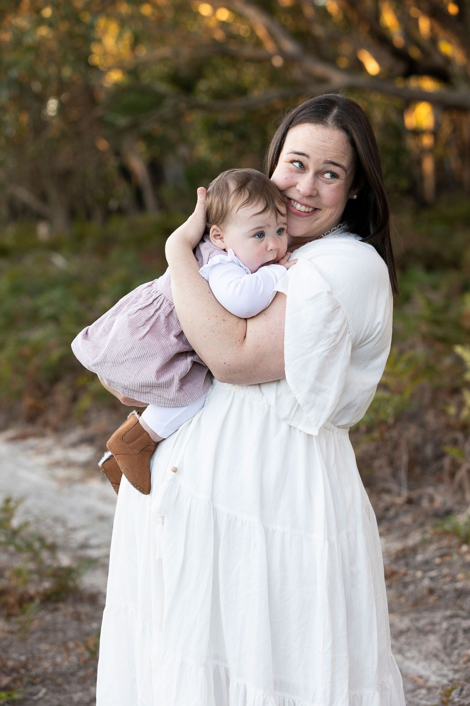 A tender embrace between parent and child in white dresses at sunset.