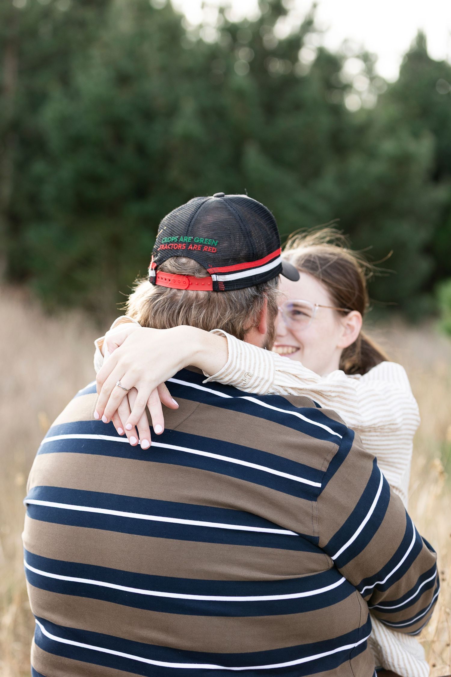 Couple embracing in field with trees in background during sunset.
