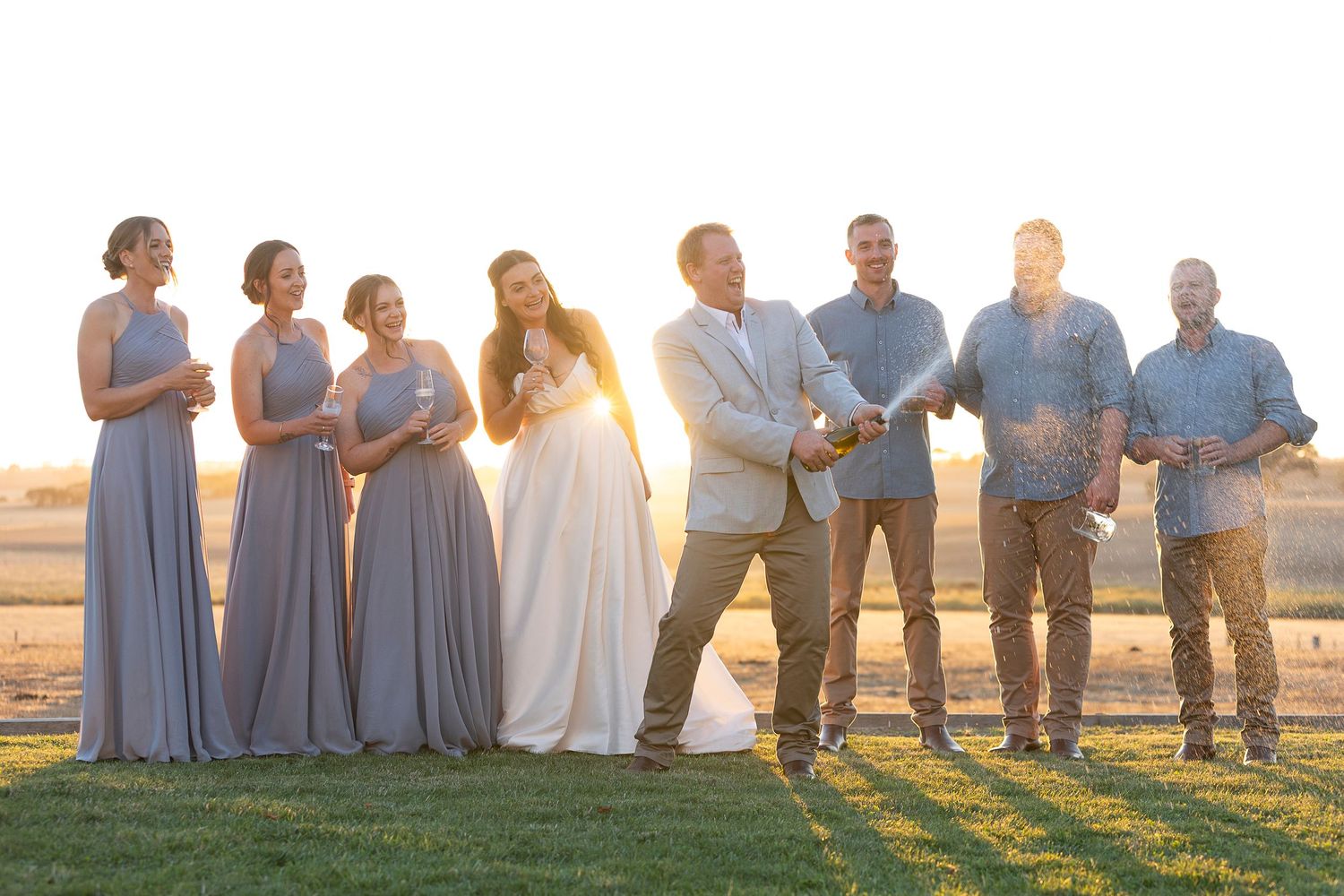 Wedding party lined up against golden sunset sky in coordinated blue and white attire.
