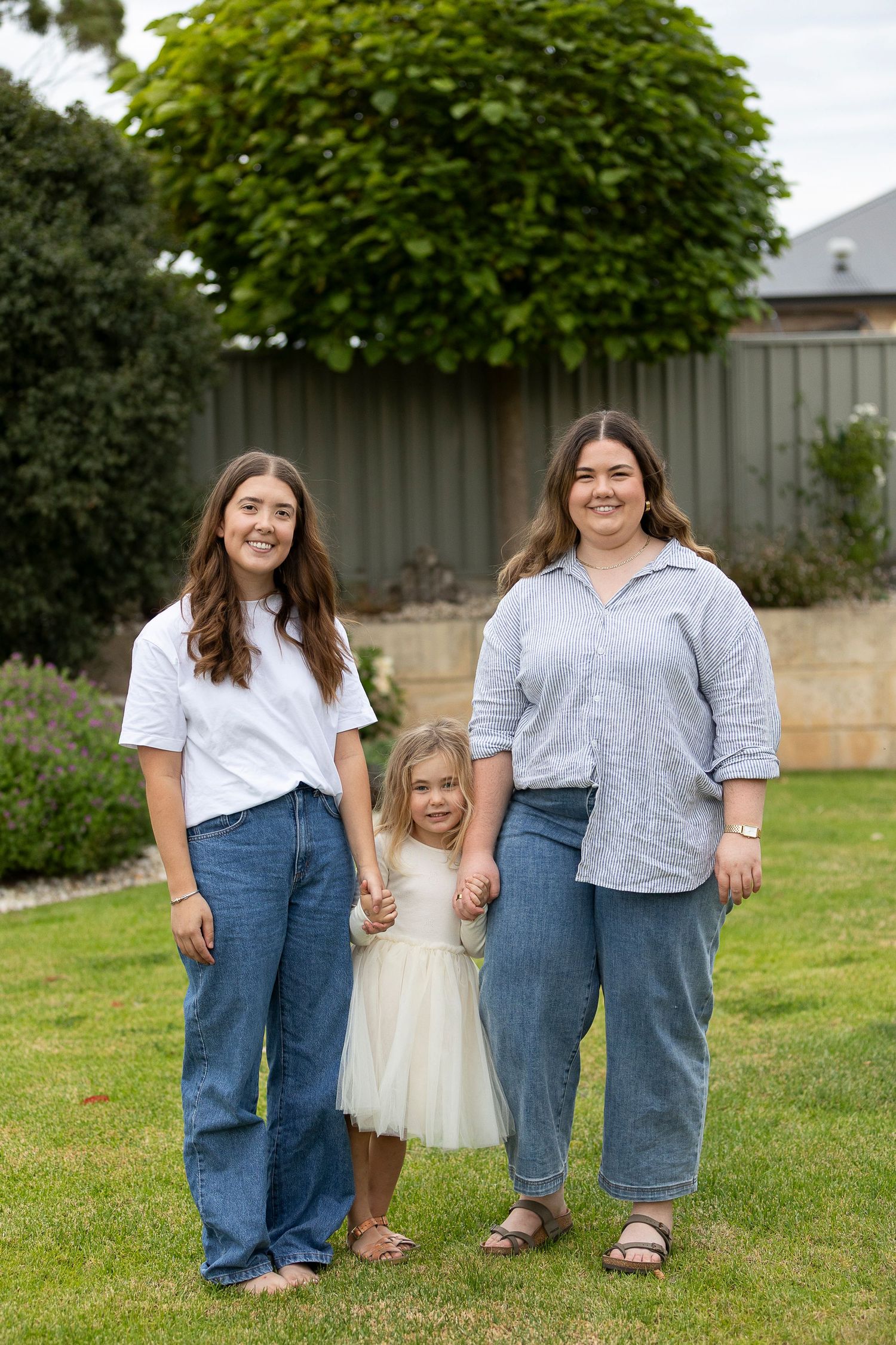 Three generations pose together on a green lawn with a fence backdrop.