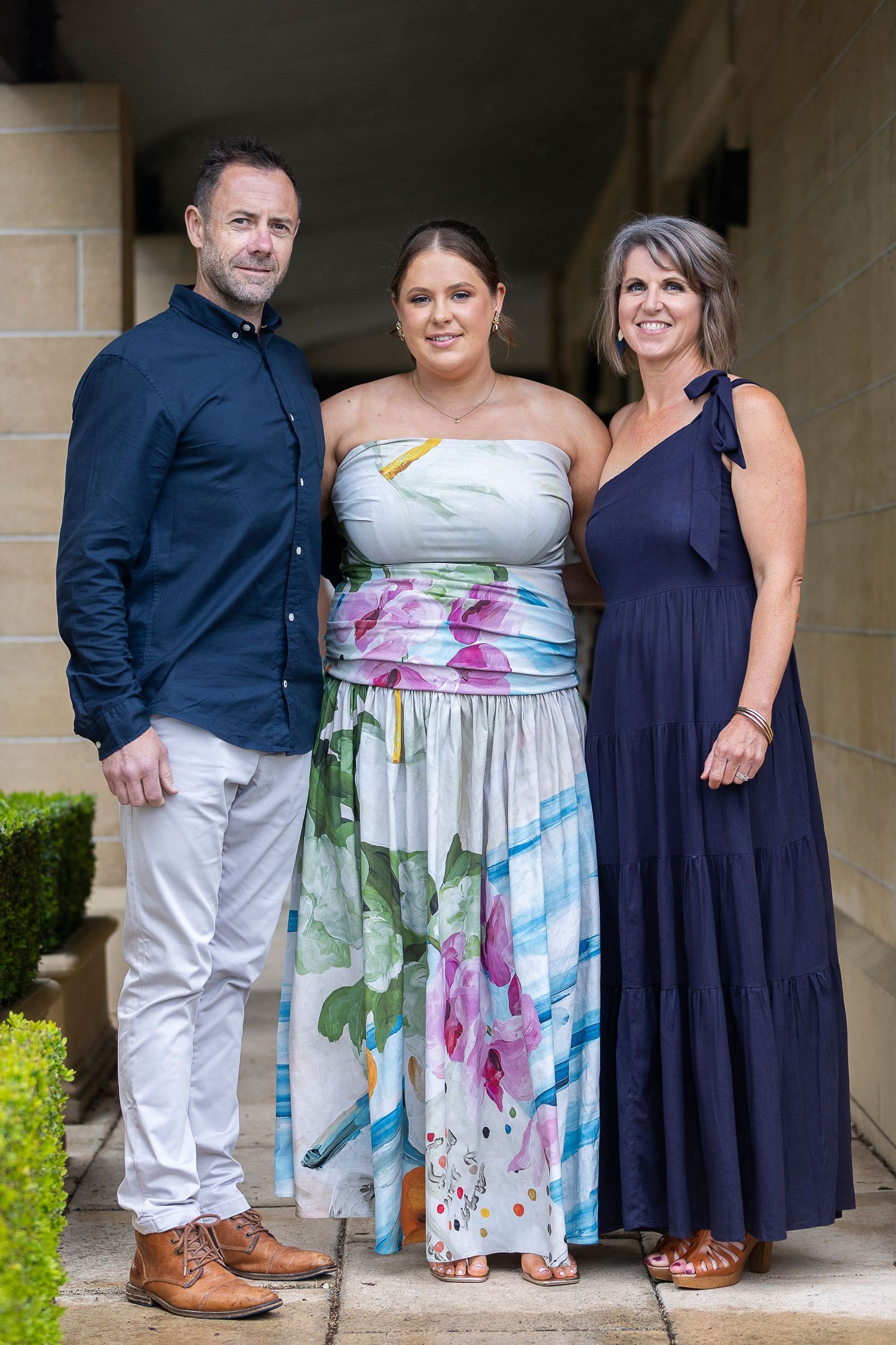 Formal group photo with mix of navy and floral dresses in garden setting.