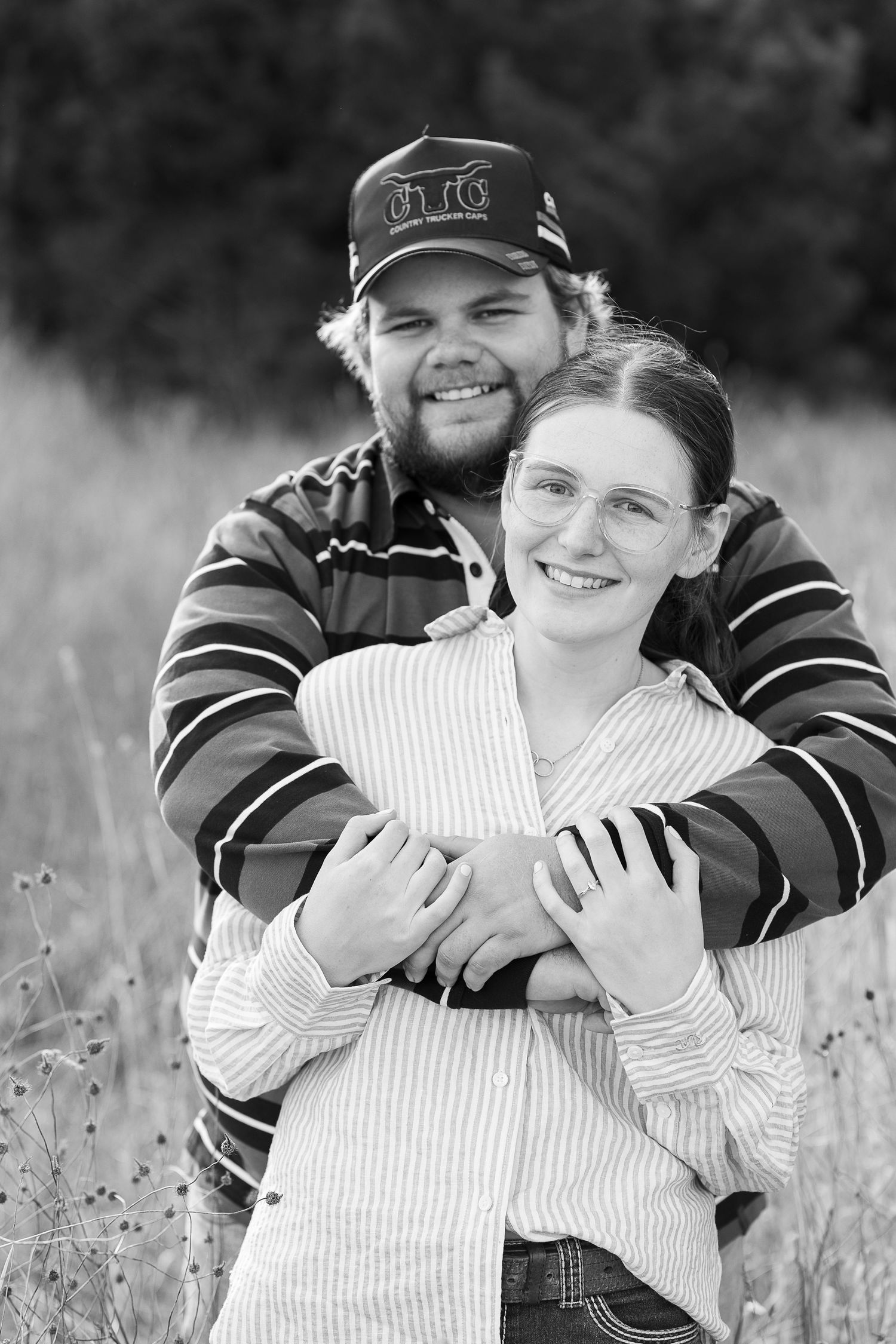 Couple shares intimate embrace in black and white photo in meadow.