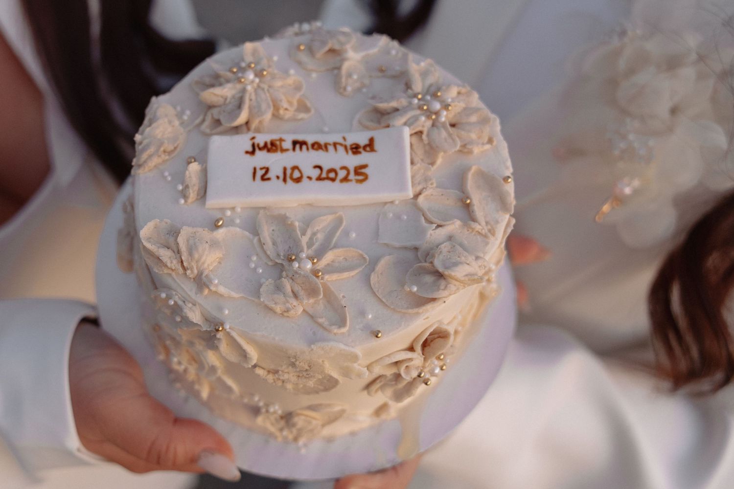 A white wedding cake decorated with delicate floral designs and a date label.