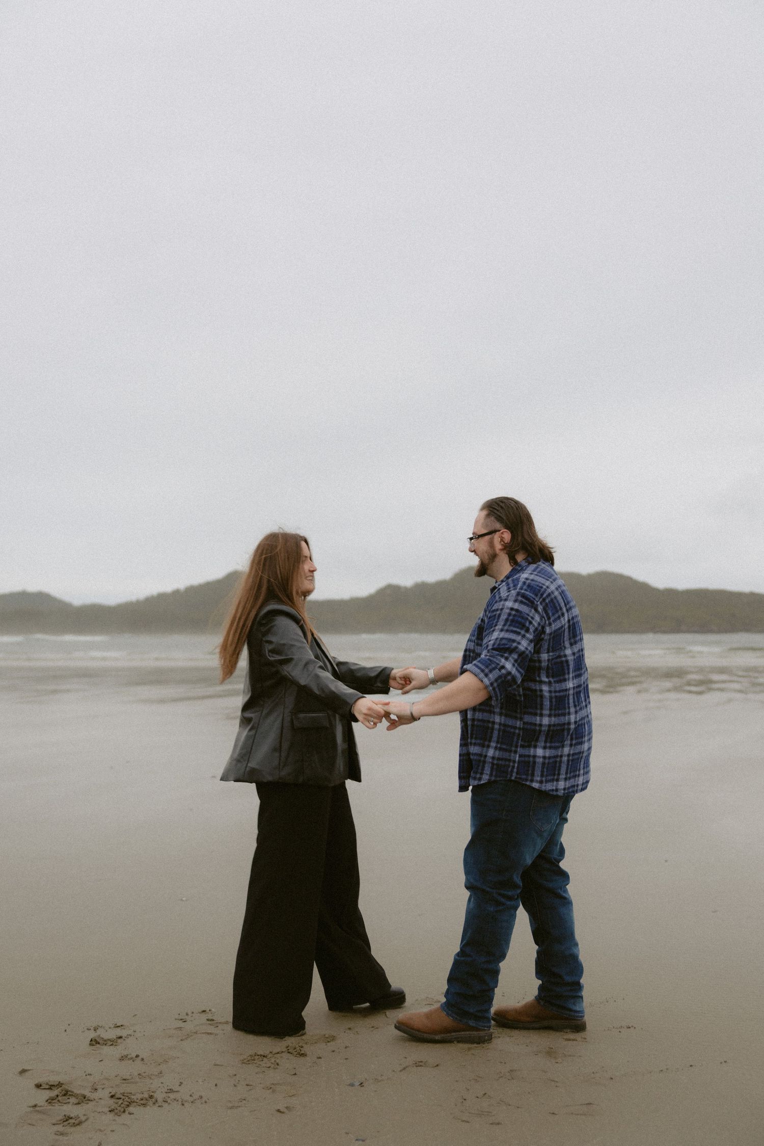 Newly engaged couple dancing on a moody Pacific Northwest beach in Tofino