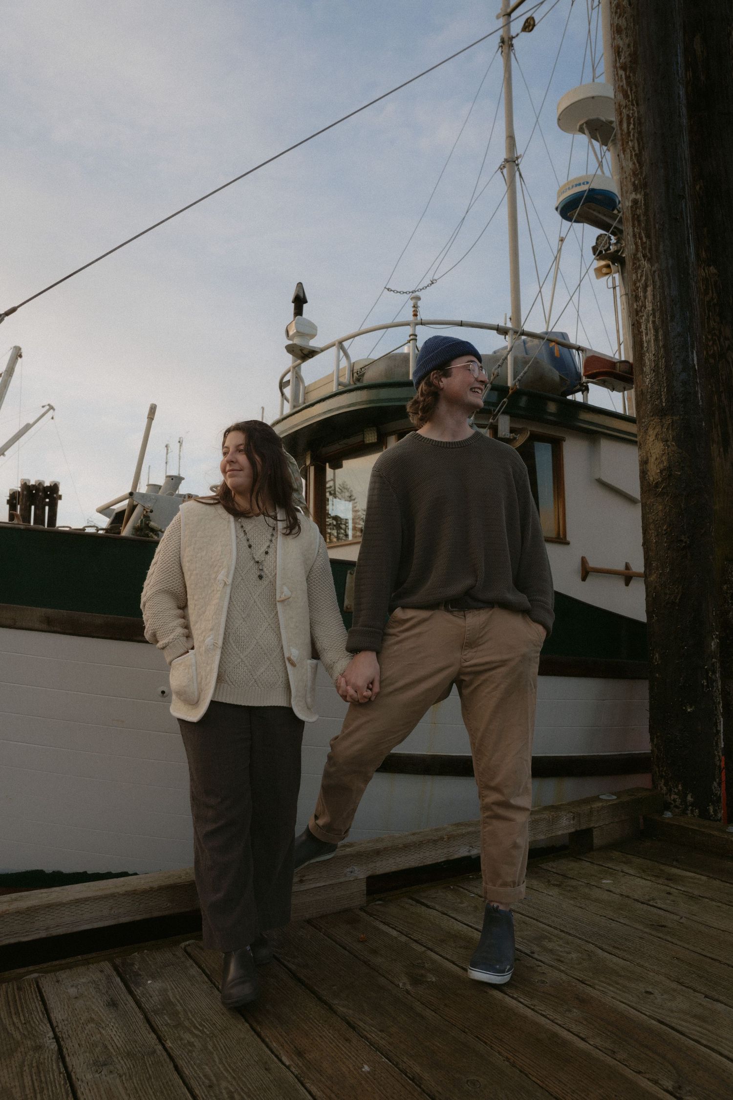 Two people walking hand in hand on a wooden dock surrounded by moored boats.