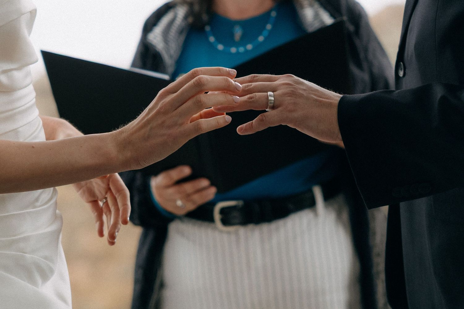 Close-up of a couple exchanging wedding rings during a ceremony, officiant holding a book in the background.