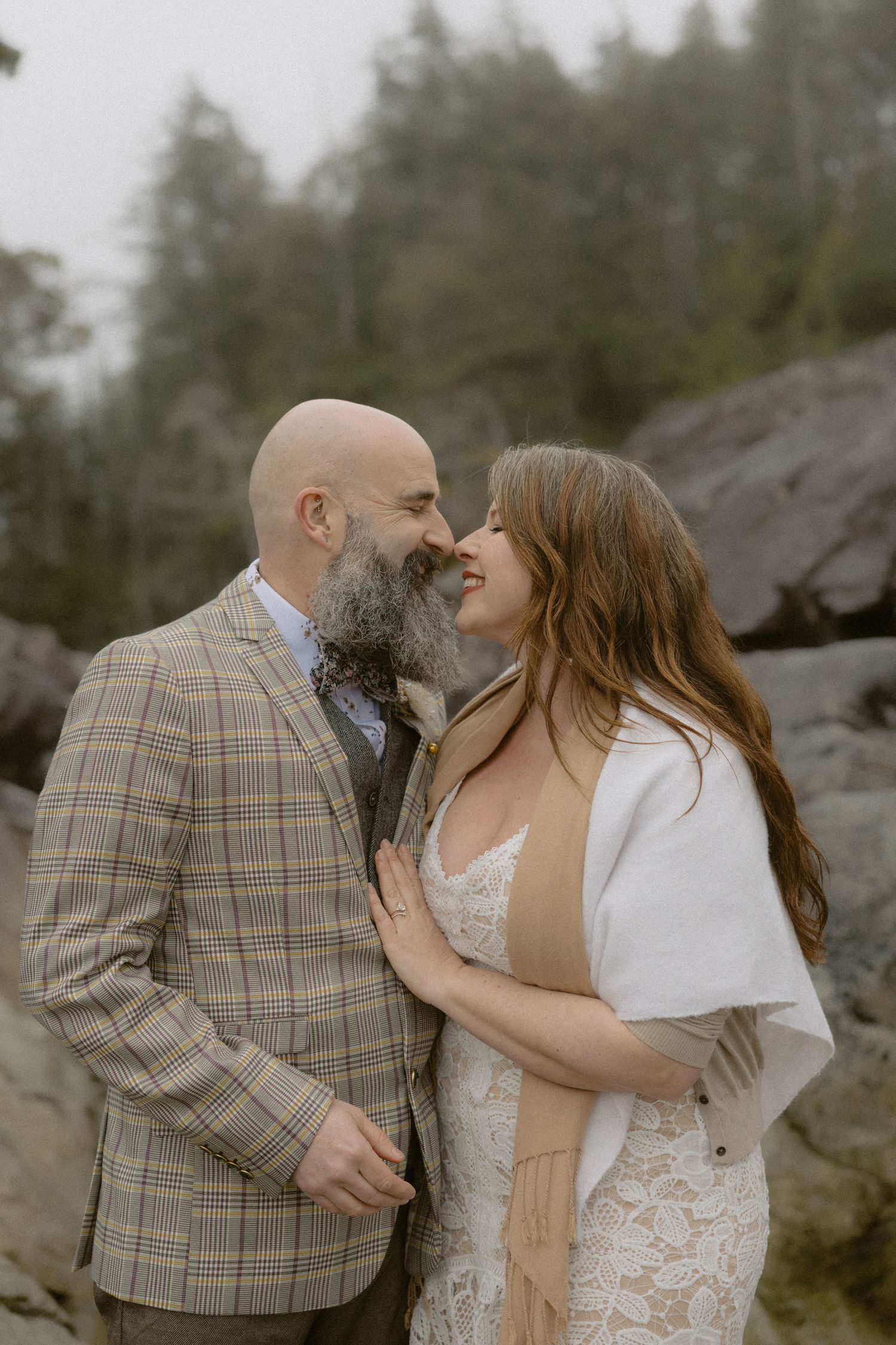 A romantic moment between newlyweds wearing a plaid suit and lace dress against rocky backdrop.