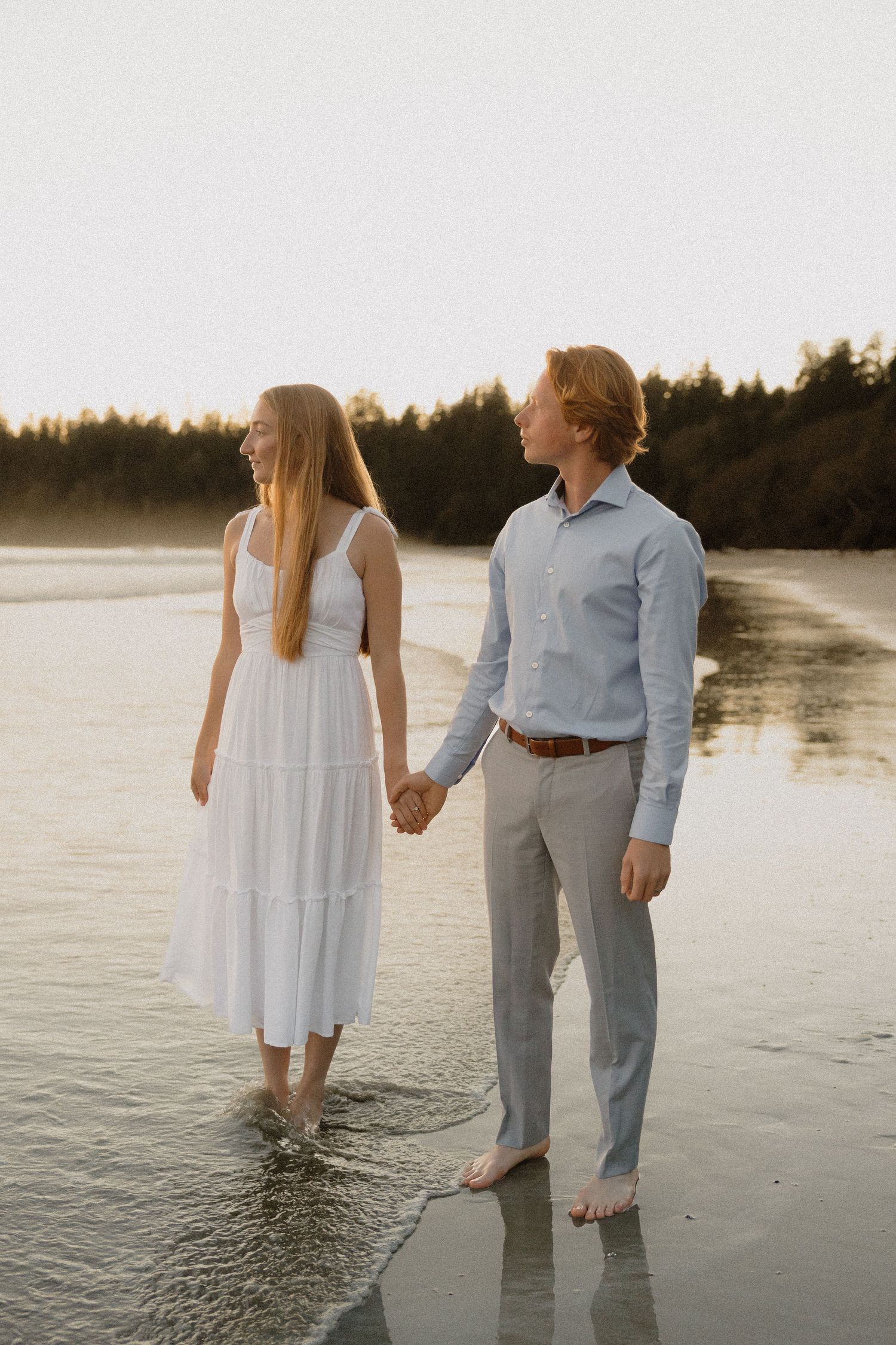Ucluelet elopement couple wading in shallow ocean water at sunset at Florencia Bay, wearing white and blue outfits