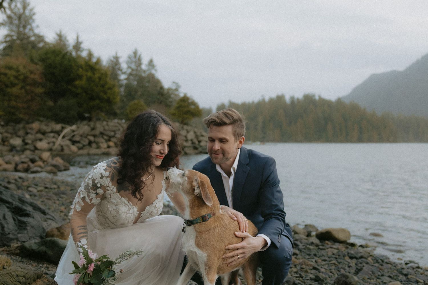 A joyful moment shared between a couple and their dog on a scenic rocky beach.
