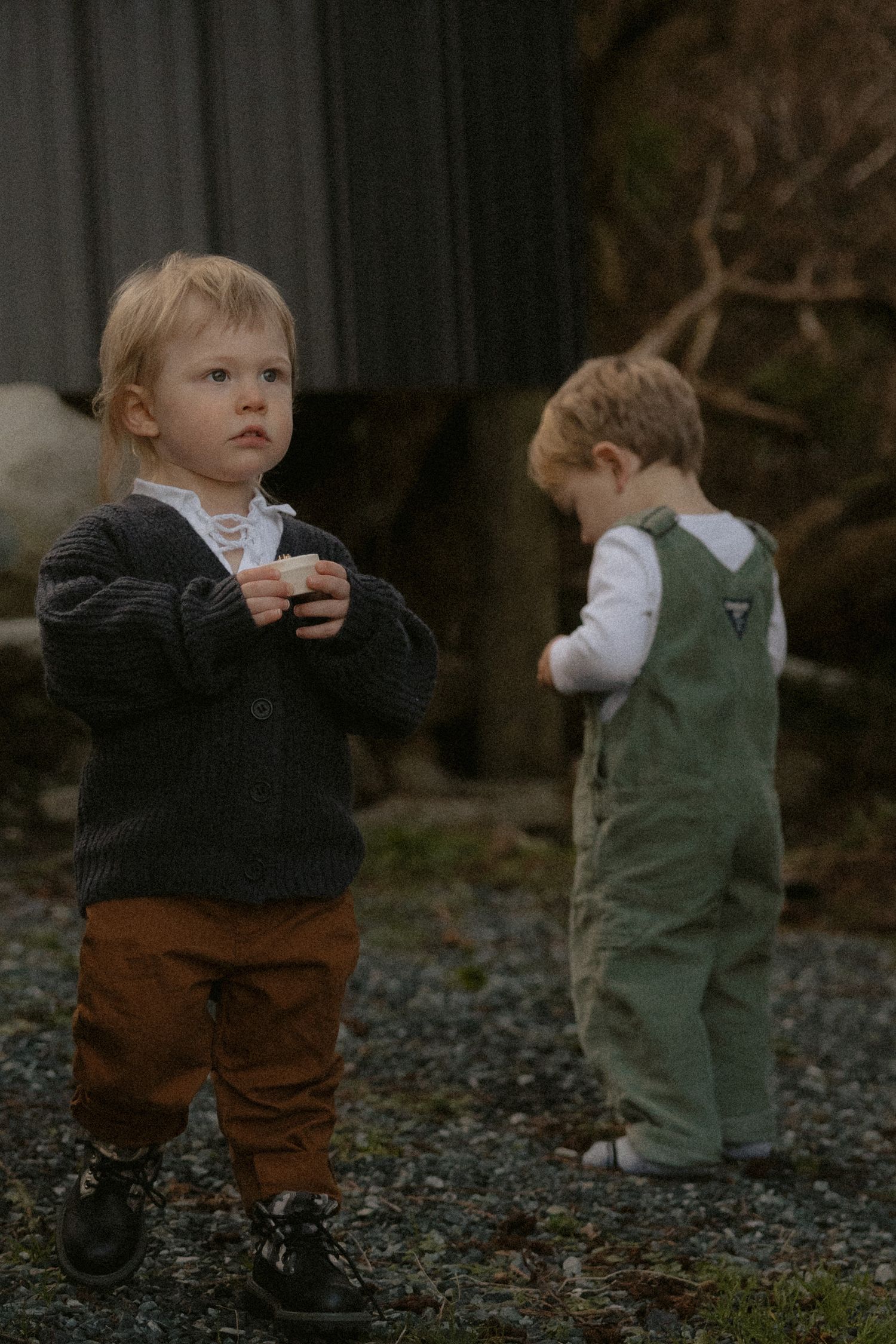 Small child in green overalls and dark sweater exploring rocky outdoor terrain.