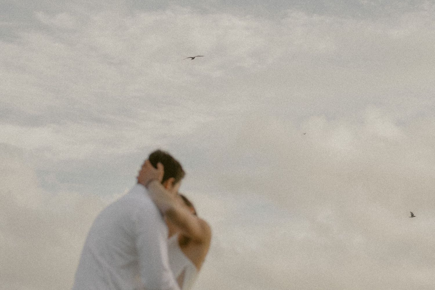 A tender wedding moment captured against an overcast sky at the beach.