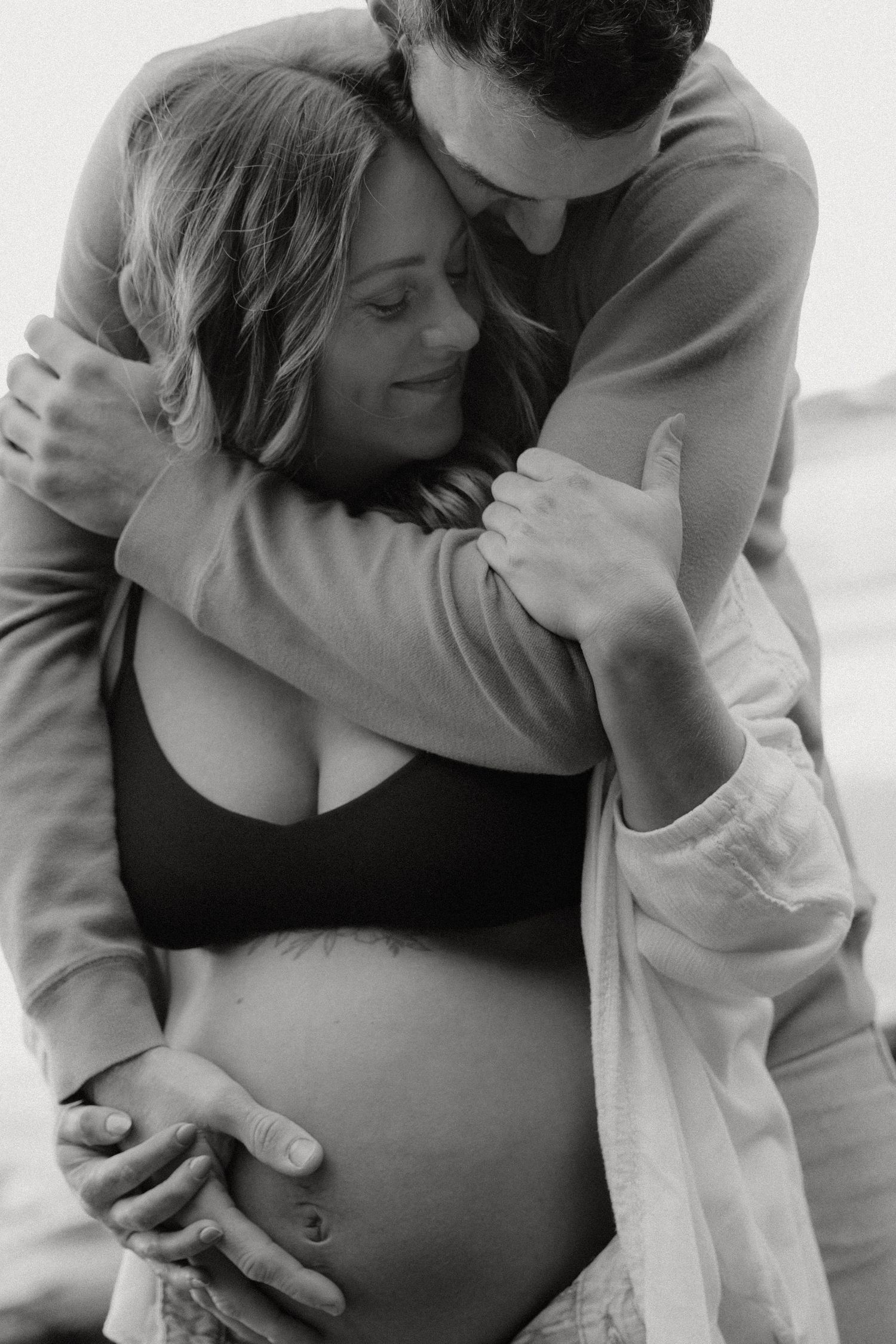 Intimate maternity photos showing loving embraces on a cloudy beach.