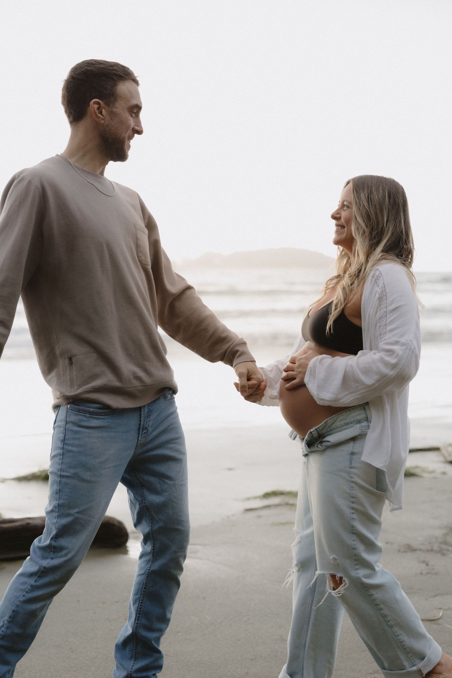 Playful couple dances together during their beach maternity photoshoot.