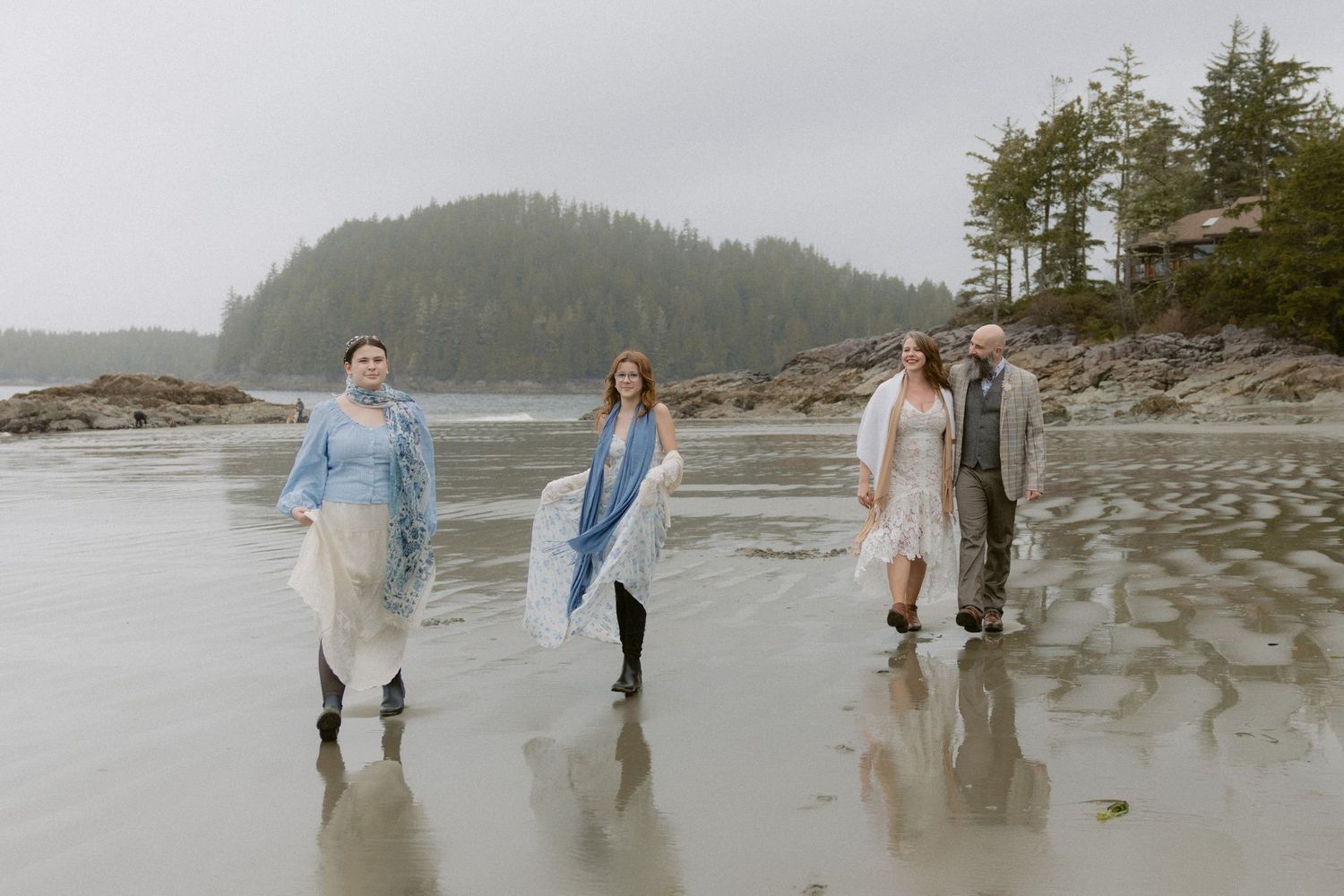 People walking along a misty Pacific Northwest beach with mountains and forest in the background.