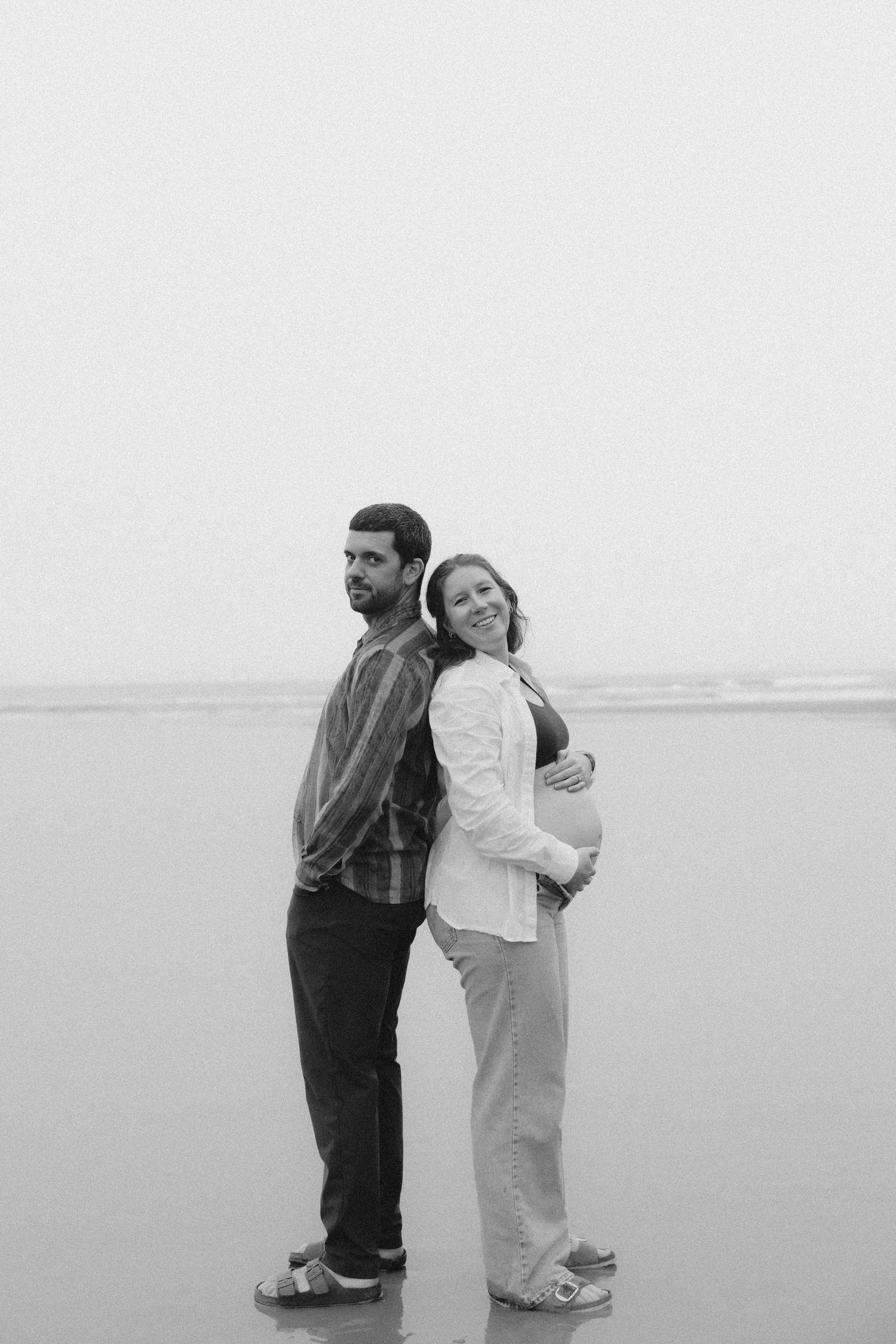 A couple embraces while standing in shallow water on an overcast day.