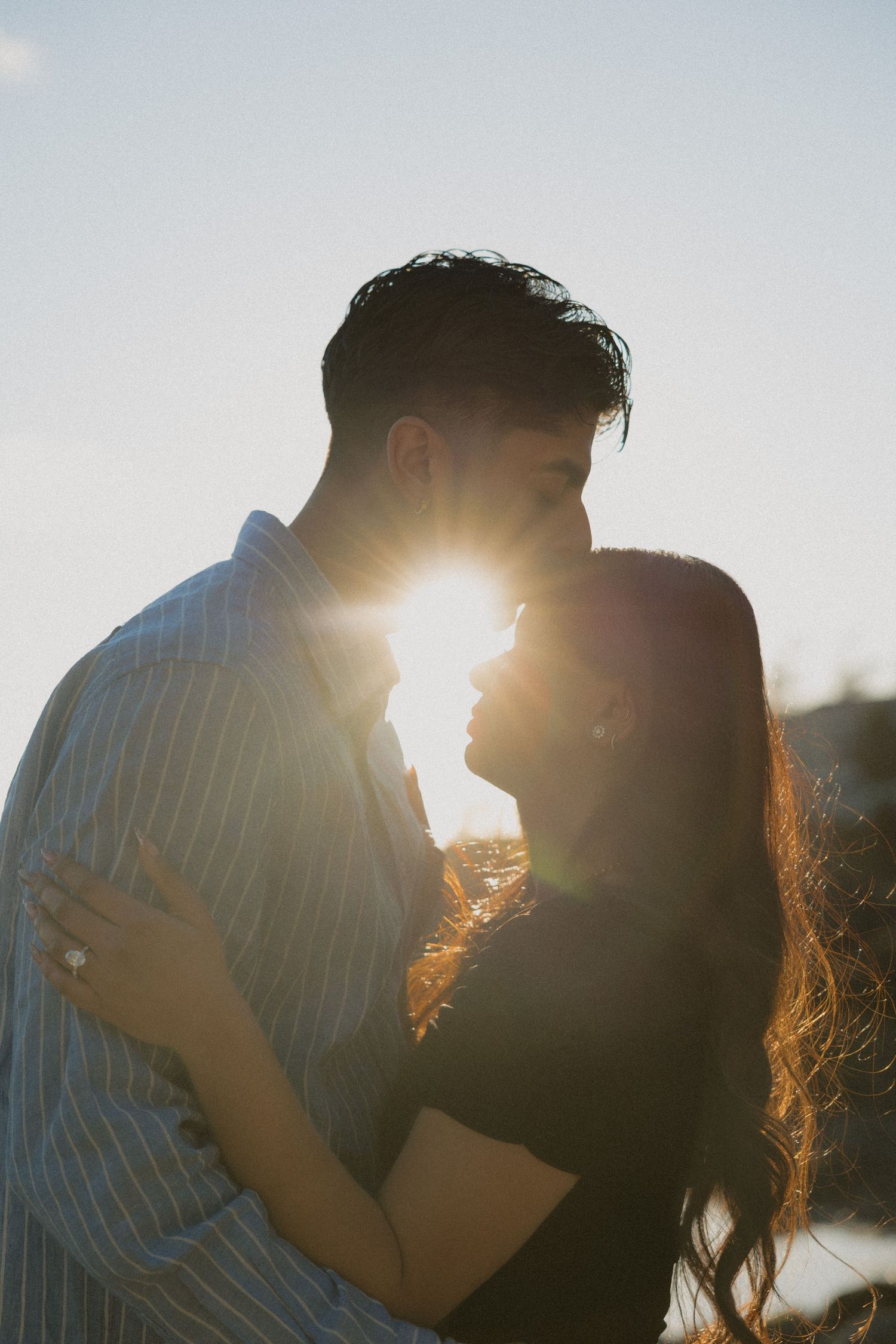 Romantic couple silhouetted against a bright sunburst at golden hour, sharing an intimate moment outdoors.